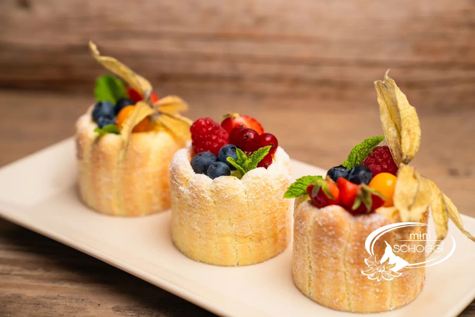 Drei Beeren-Charlotten mit Himbeeren, Heidelbeeren und Physalis auf weisser Platte