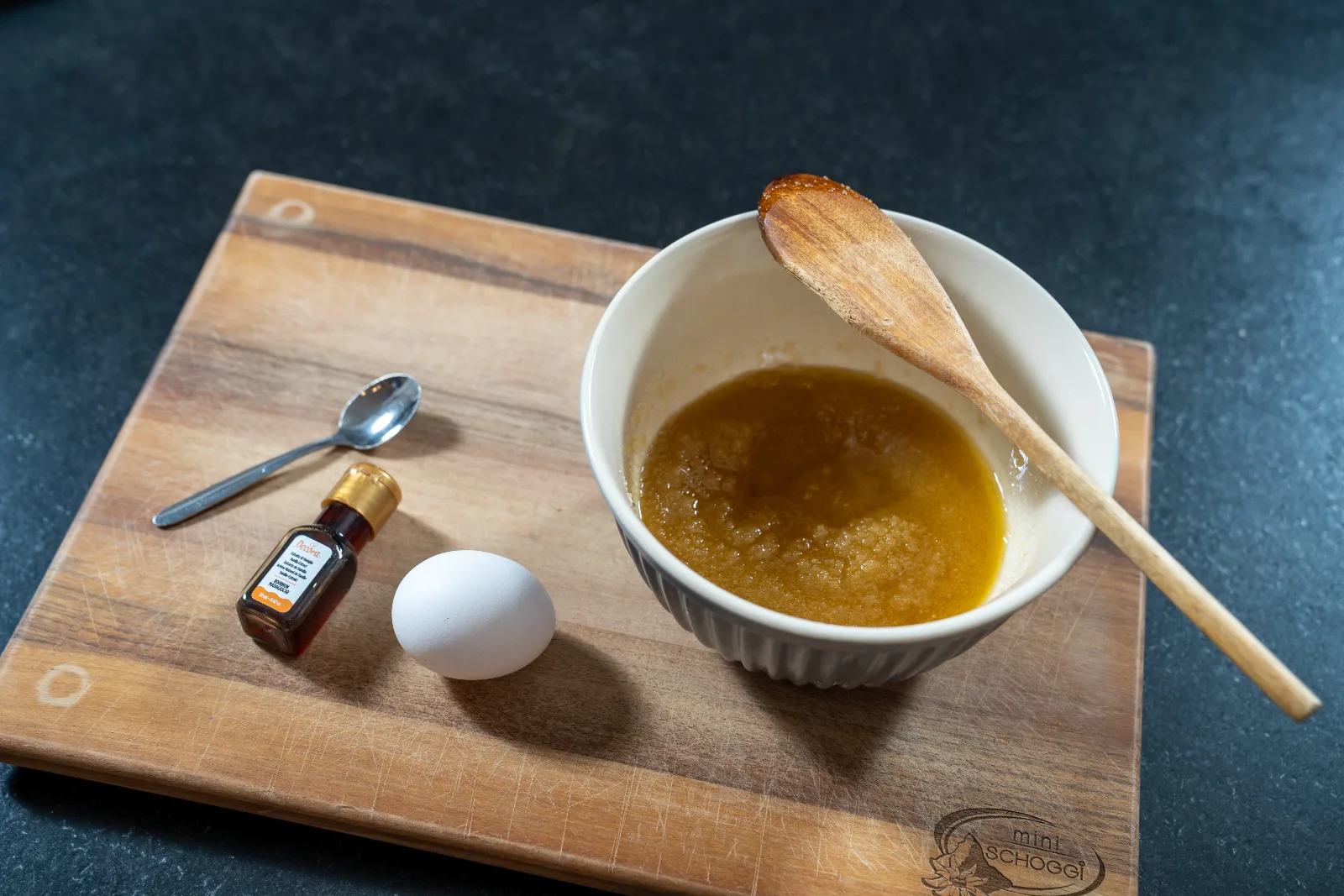 Butter-sugar mixture with a wooden spoon, next to egg and natural extract