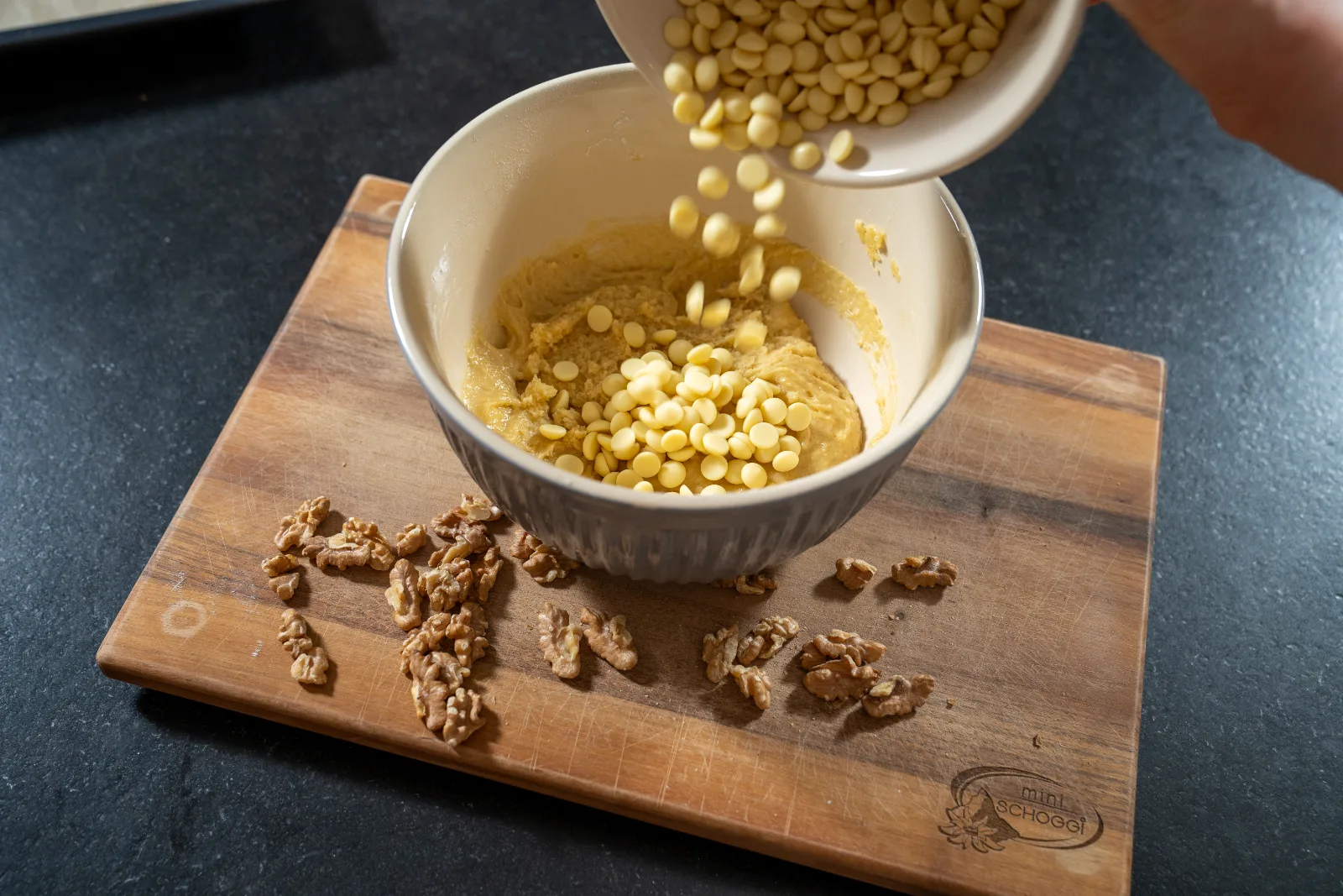 White chocolate chips being added to the blondie dough, next to chopped walnuts