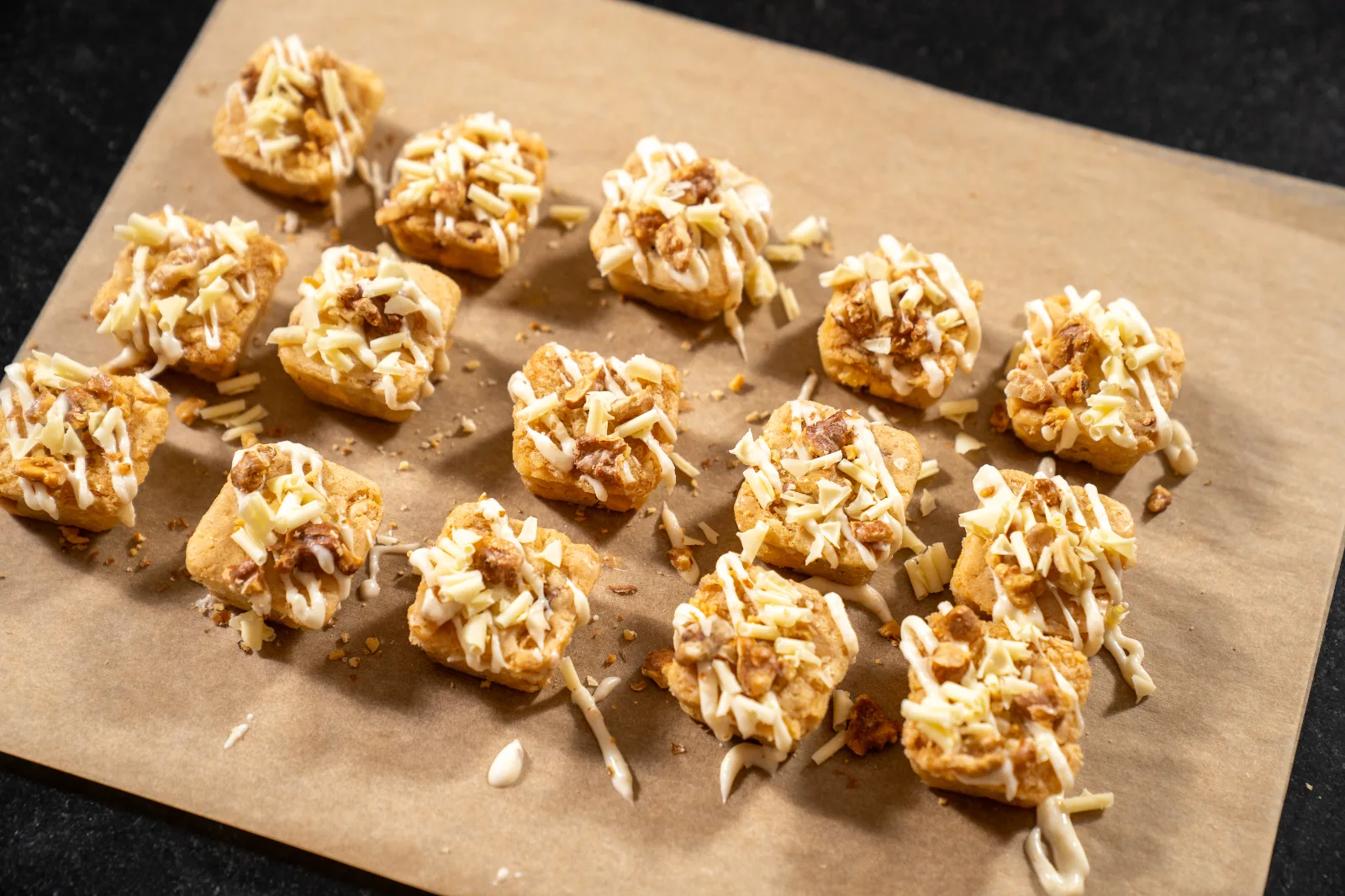 Blondies being decorated with white Ganache from a piping bag, next to walnuts and chocolate curls