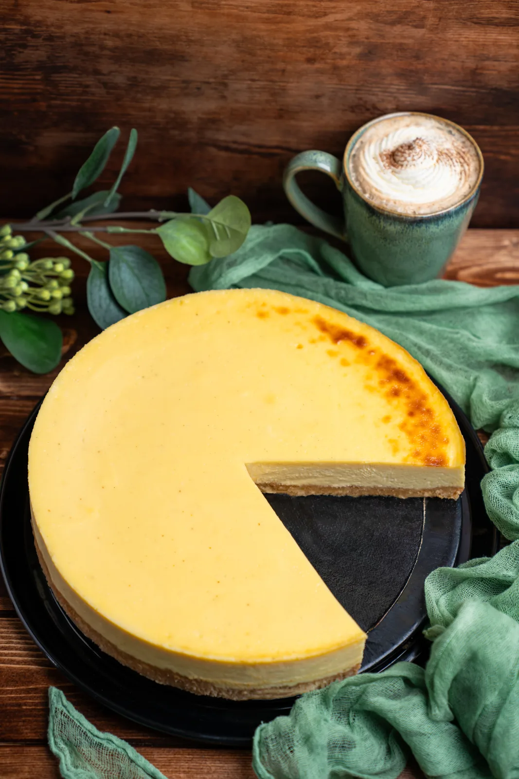 Sliced cheesecake with a golden surface and biscuit base on a dark plate