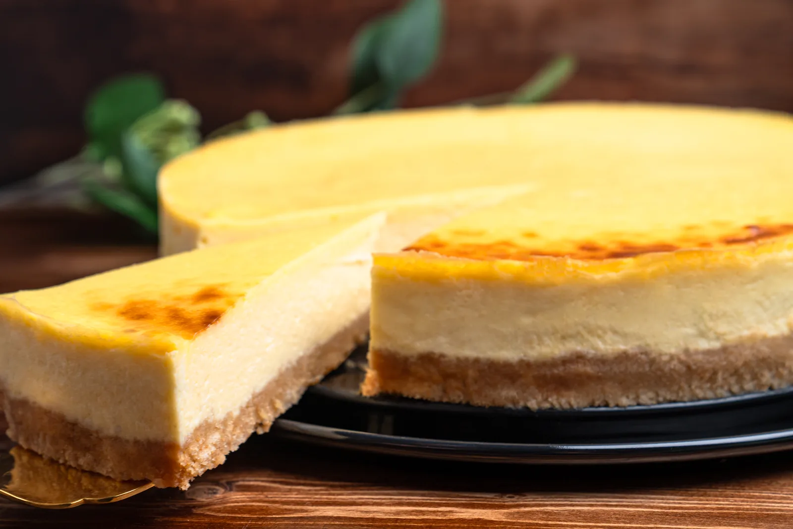 Sliced cheesecake with a golden surface and biscuit base on a dark plate