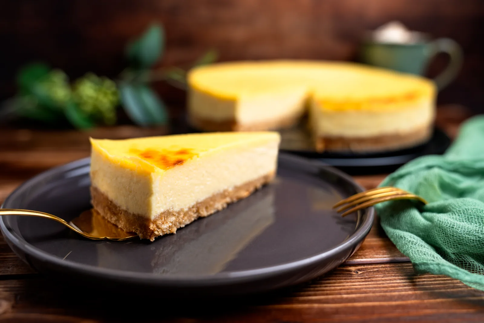 Sliced cheesecake with a golden surface and biscuit base on a dark plate