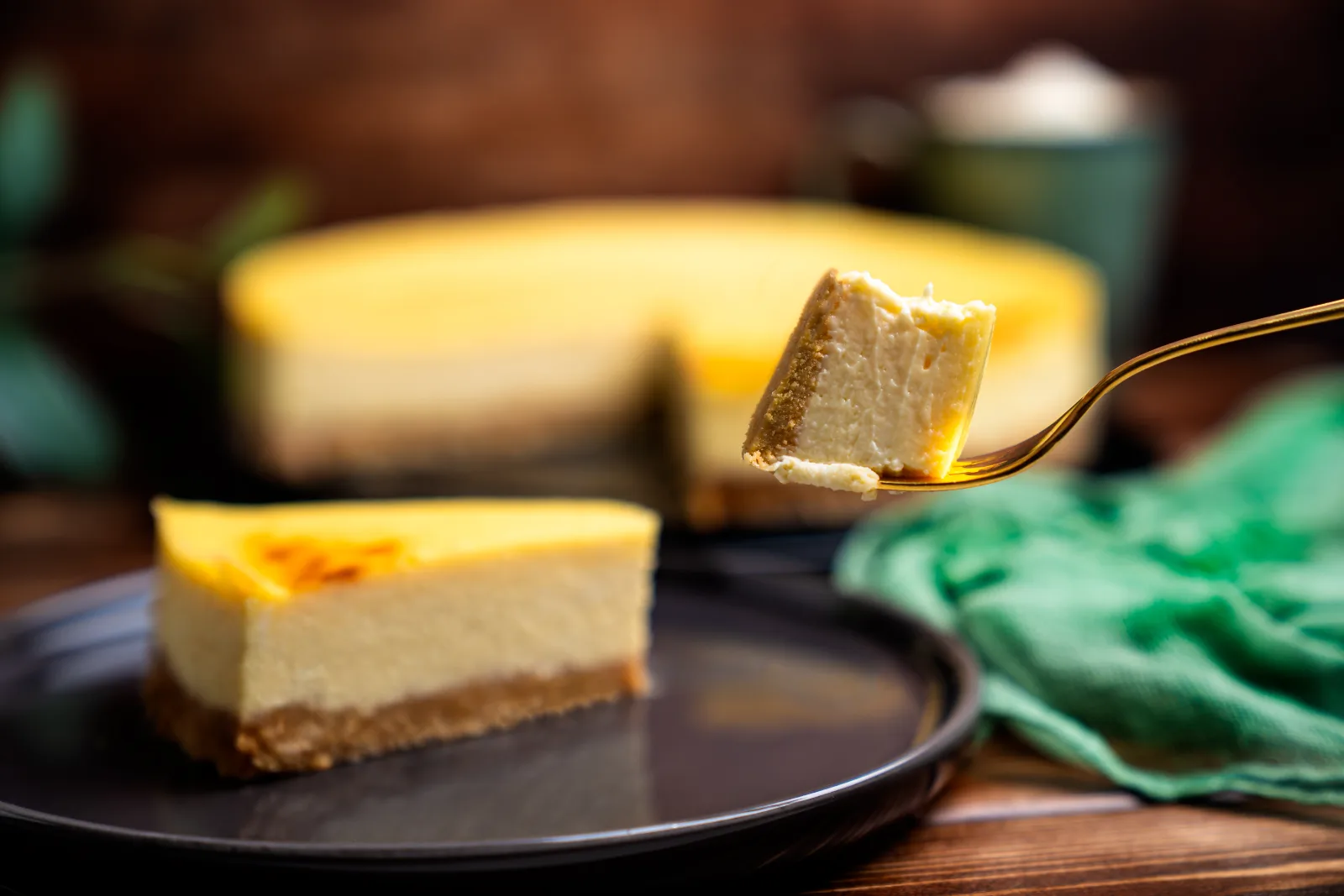 Sliced cheesecake with a golden surface and biscuit base on a dark plate