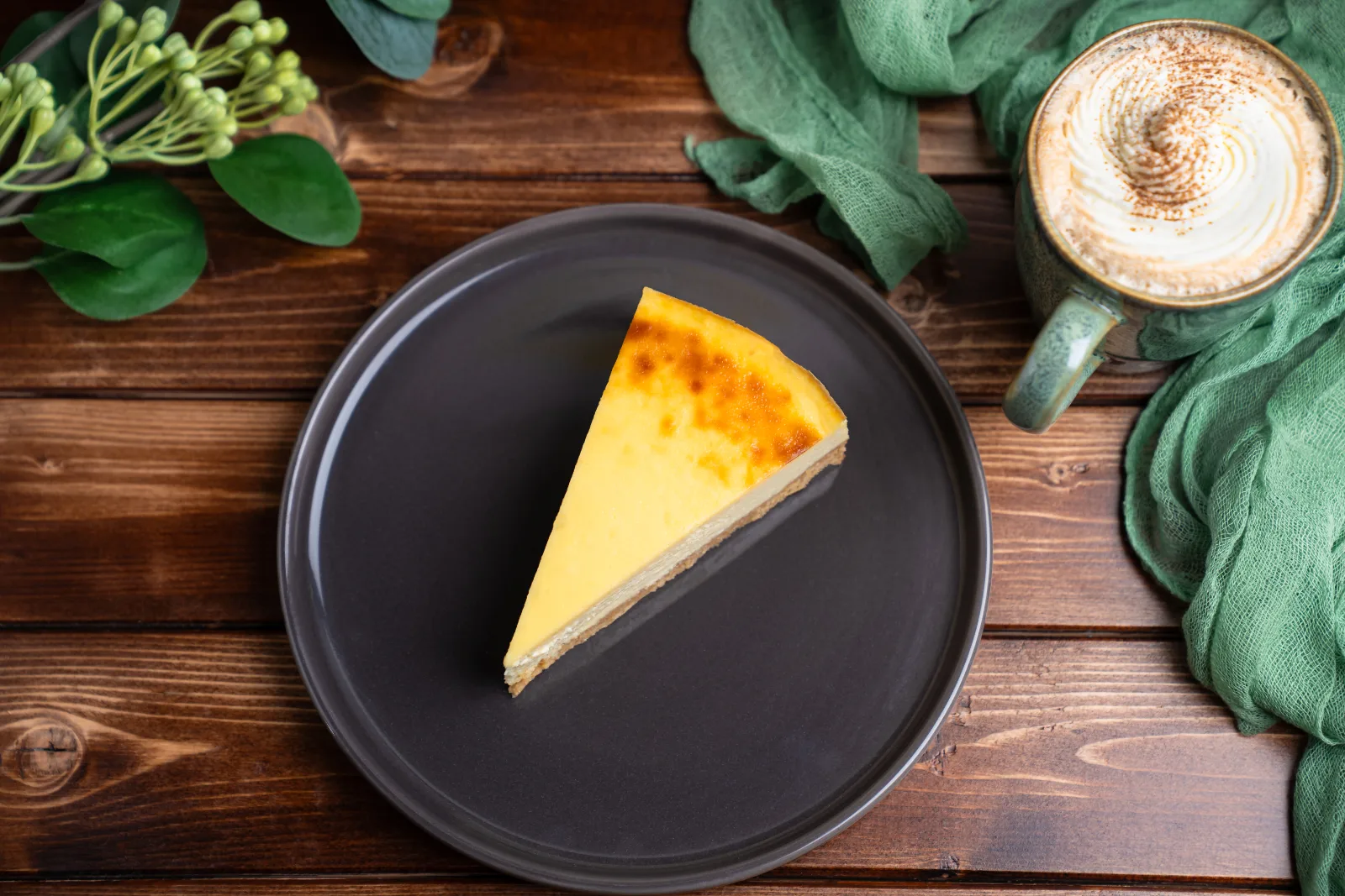 Sliced cheesecake with a golden surface and biscuit base on a dark plate