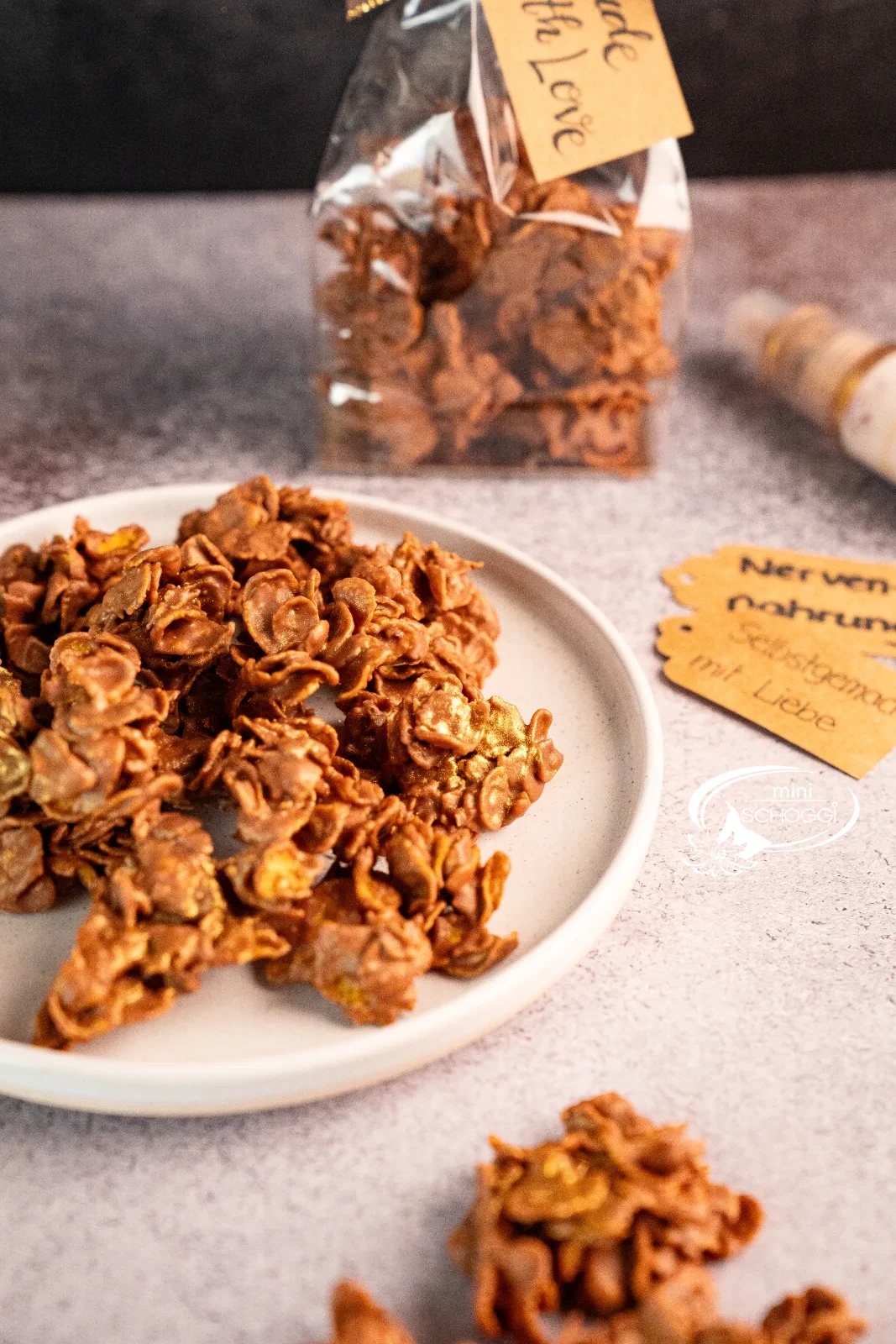 Biscotti cornflakes nel sacchetto trasparente con fiocco, accanto singoli croccantini al cioccolato