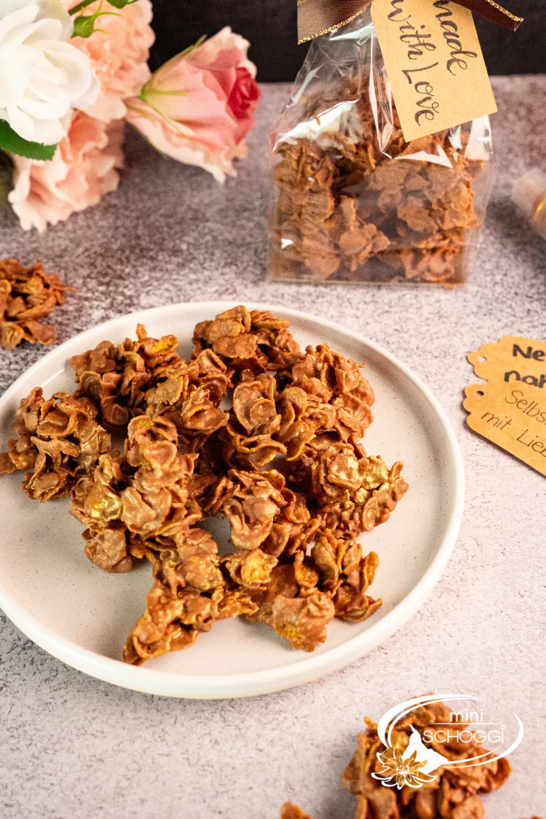 Biscotti cornflakes nel sacchetto trasparente con fiocco, accanto singoli croccantini al cioccolato