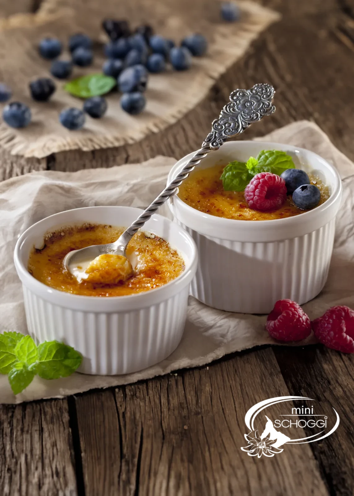 Two creme brulee with a caramelised sugar layer on a wooden table with white blossoms
