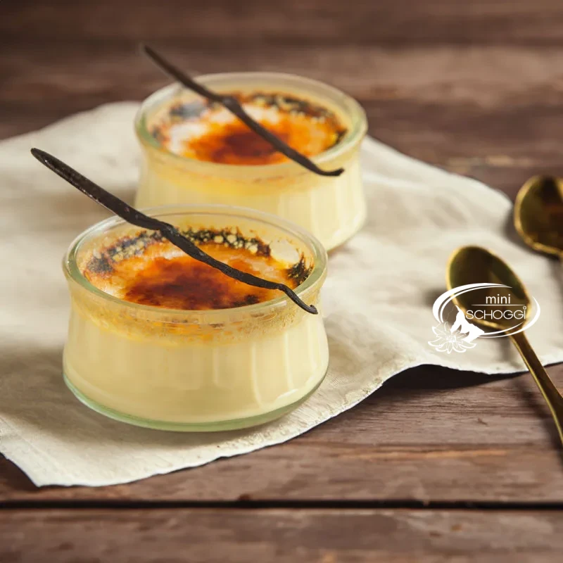 Two creme brulee with a caramelised sugar layer on a wooden table with white blossoms