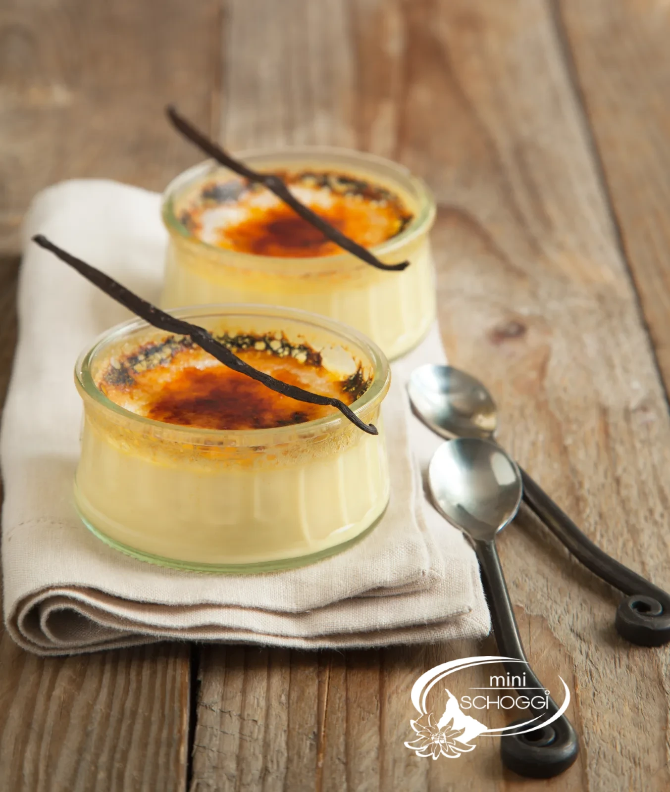 Two creme brulee with a caramelised sugar layer on a wooden table with white blossoms
