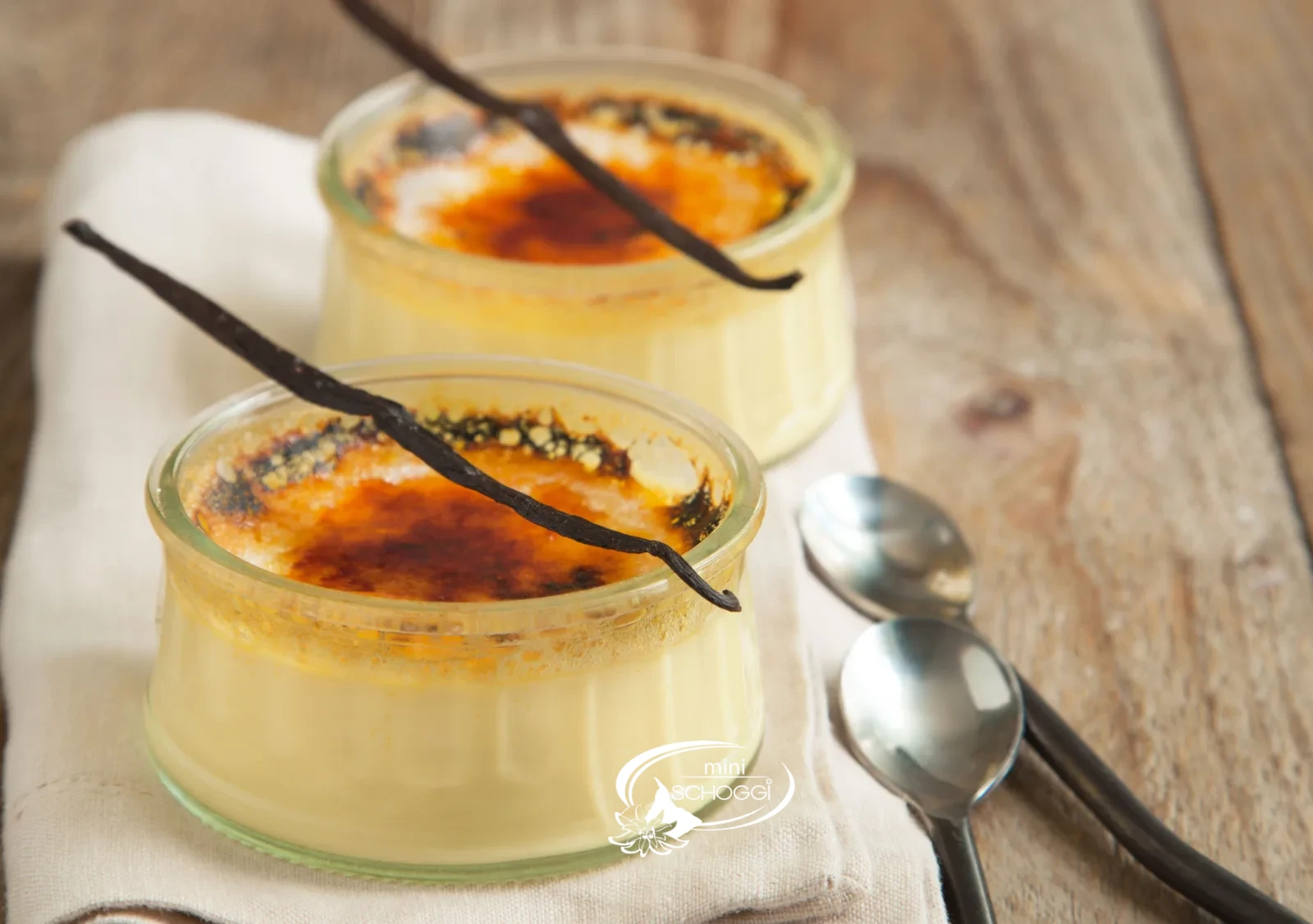 Two creme brulee with a caramelised sugar layer on a wooden table with white blossoms