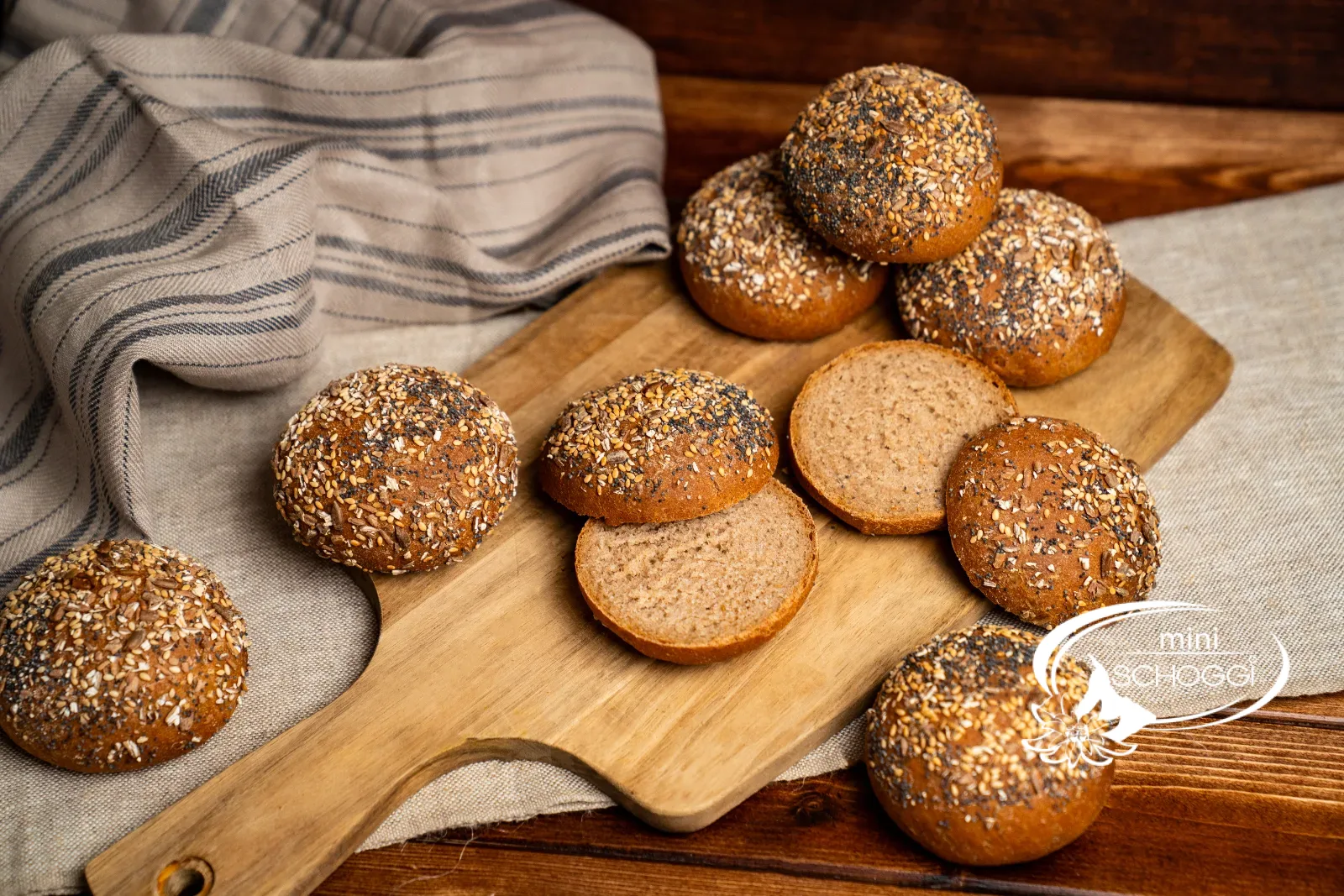 Dinkel-Vollkornbrötchen mit Körnerkruste, einige aufgeschnitten, auf einem Holzbrett