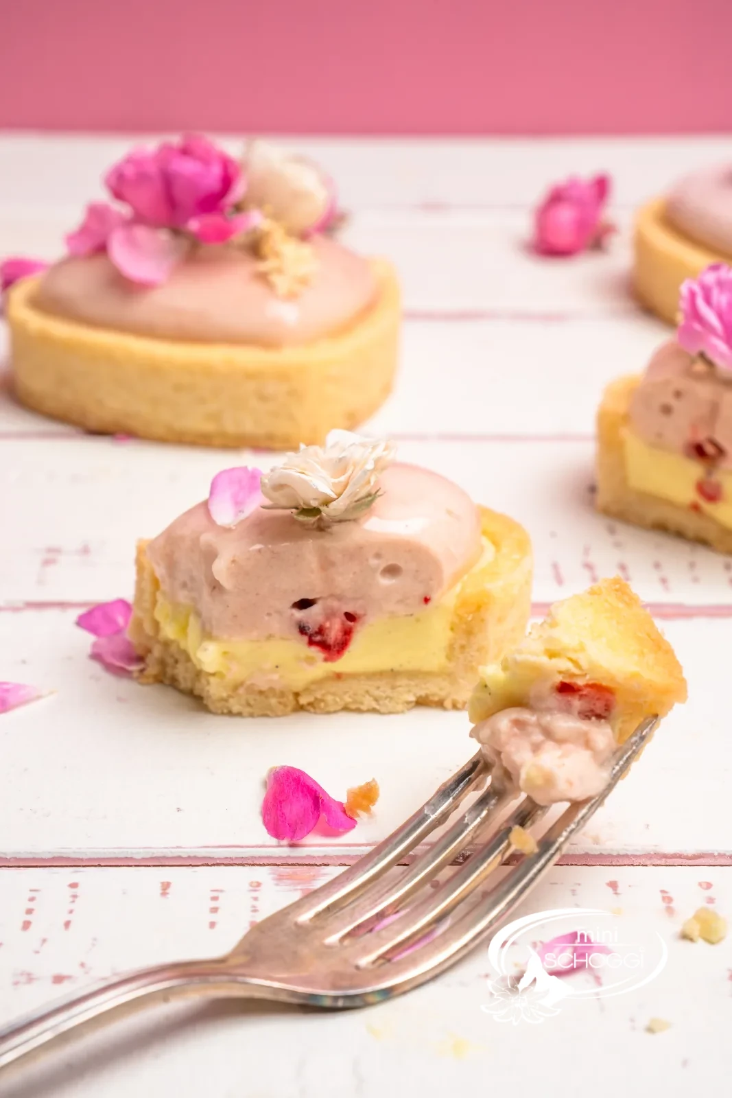 Pasticceria fragola-limone a forma di cuore con glassa rosa e boccioli di rosa commestibili