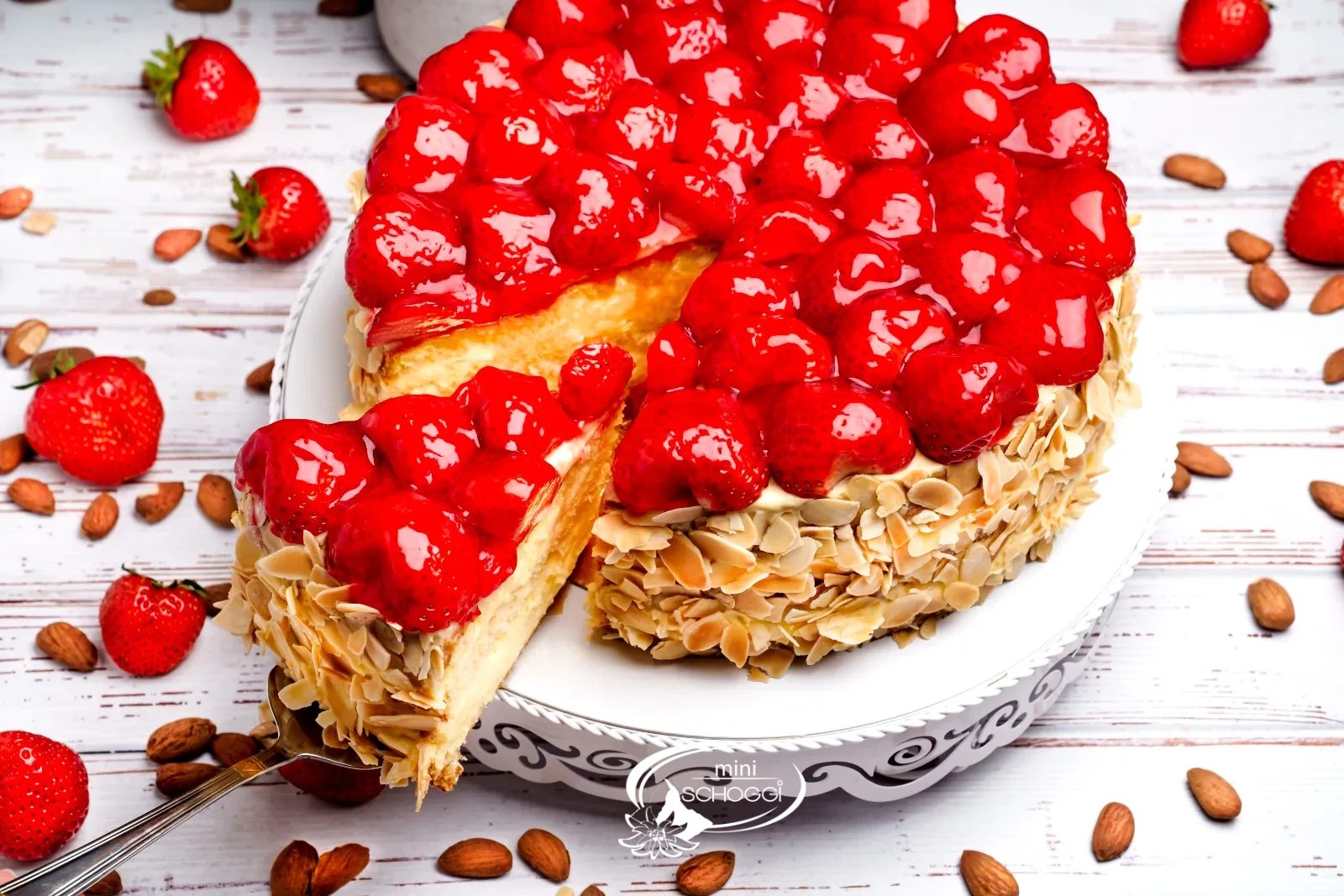 Torta di fragole tagliata con bordo di mandorle e fragole lucide