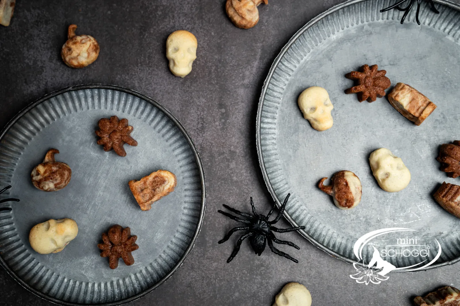 Halloween-Guetzli auf zwei Metalltellern mit Deko-Spinnen