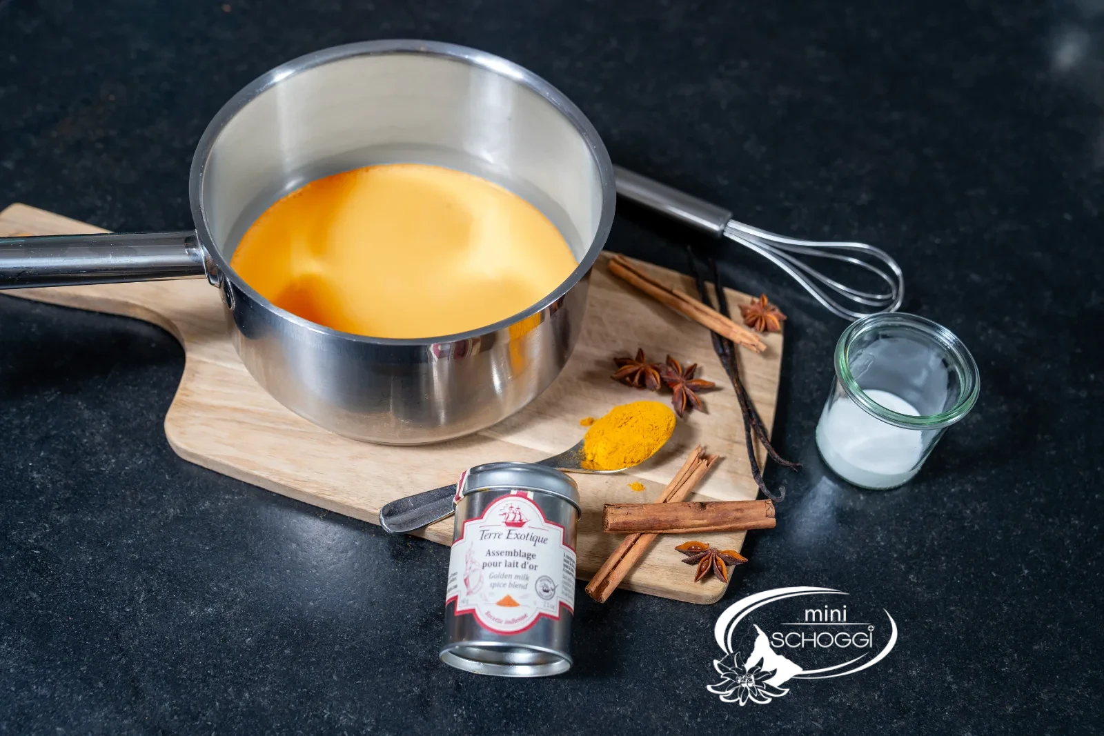 Goldene Milch im Topf mit dem Schwingbesen, daneben ein Glas Honig