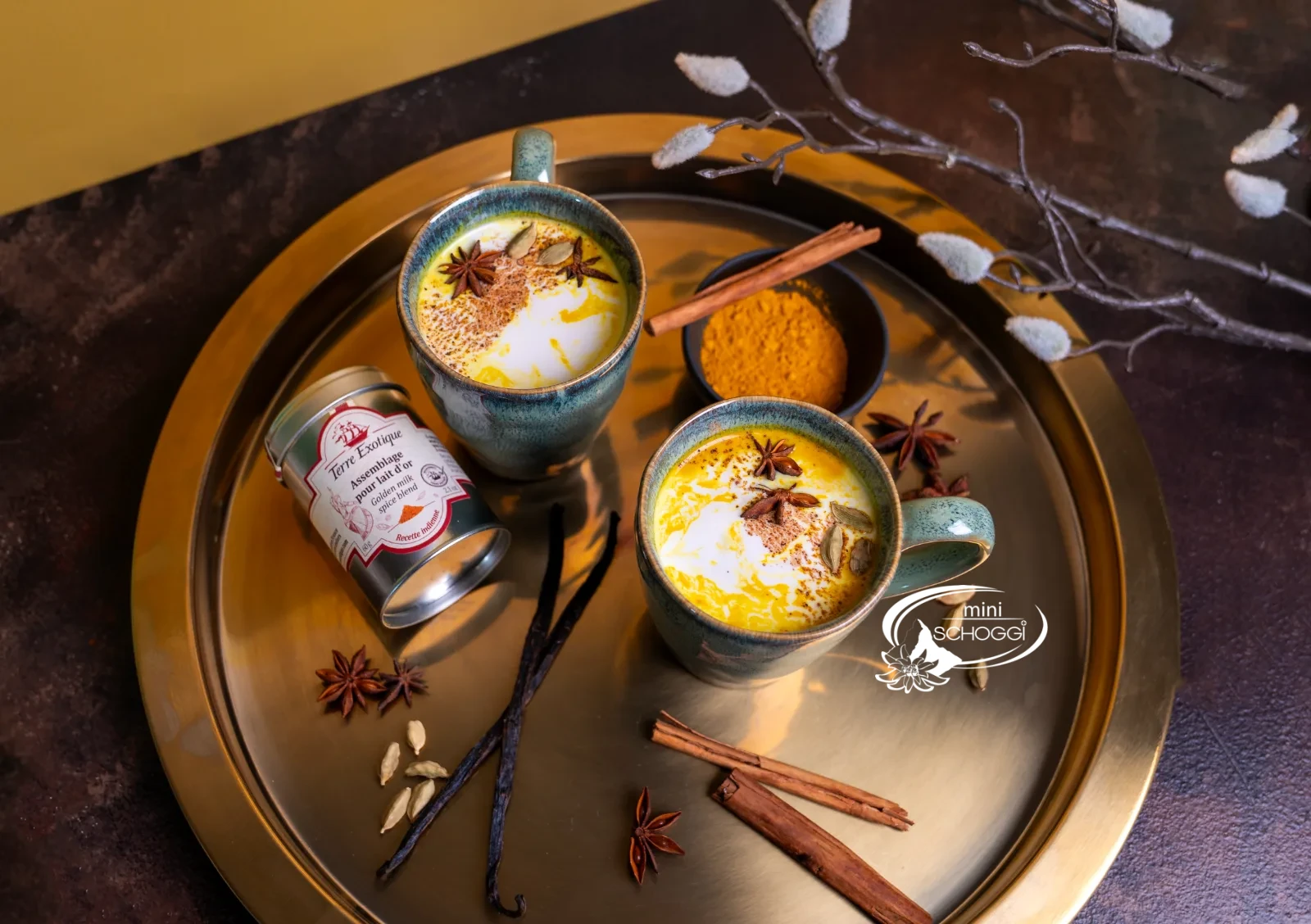 Zwei Tassen Golden Milk auf einem Messingtablett mit Zimtstangen und Gewürzmischung