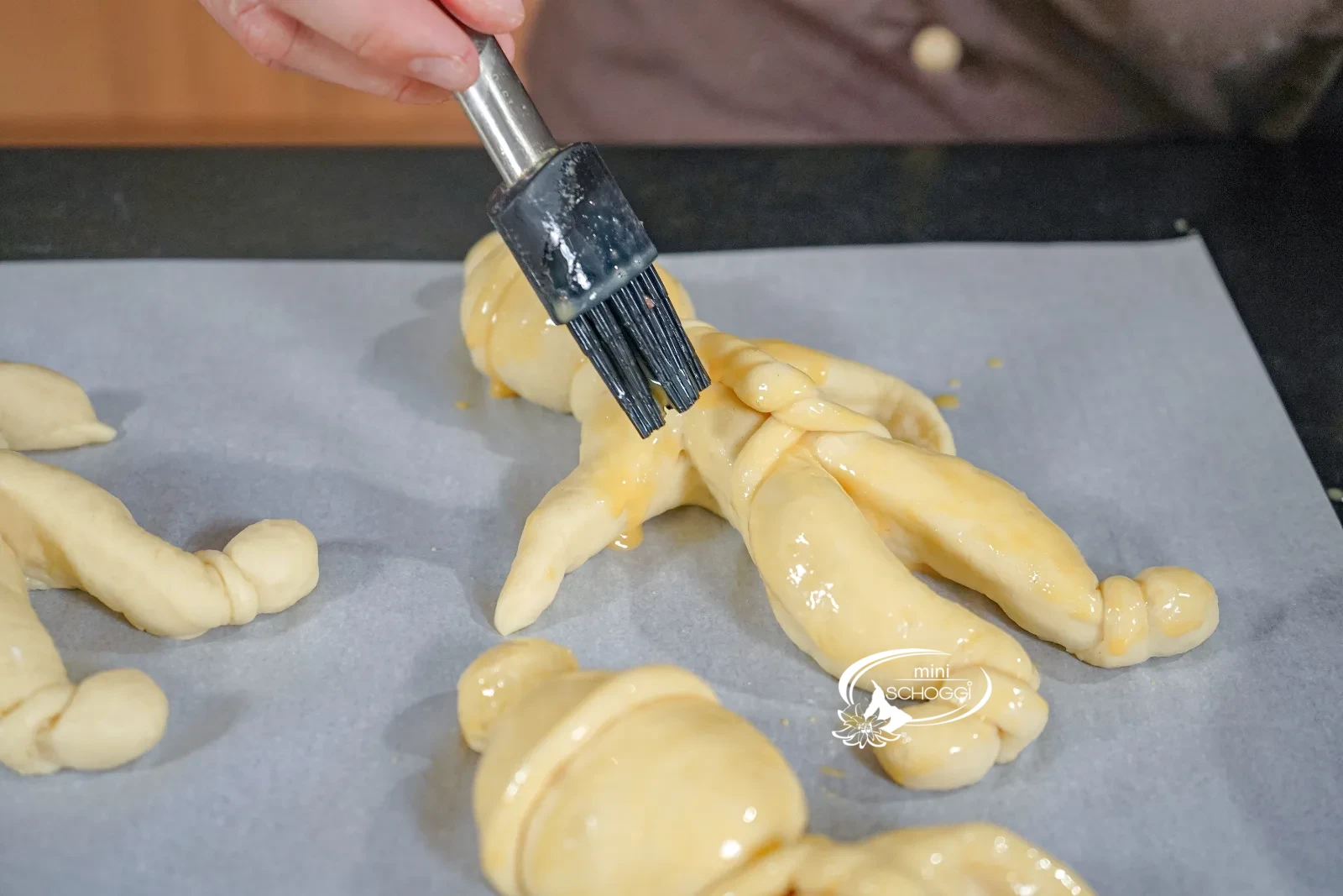 L'omino di pasta lievitata viene spennellato uniformemente con l'uovo usando il pennello