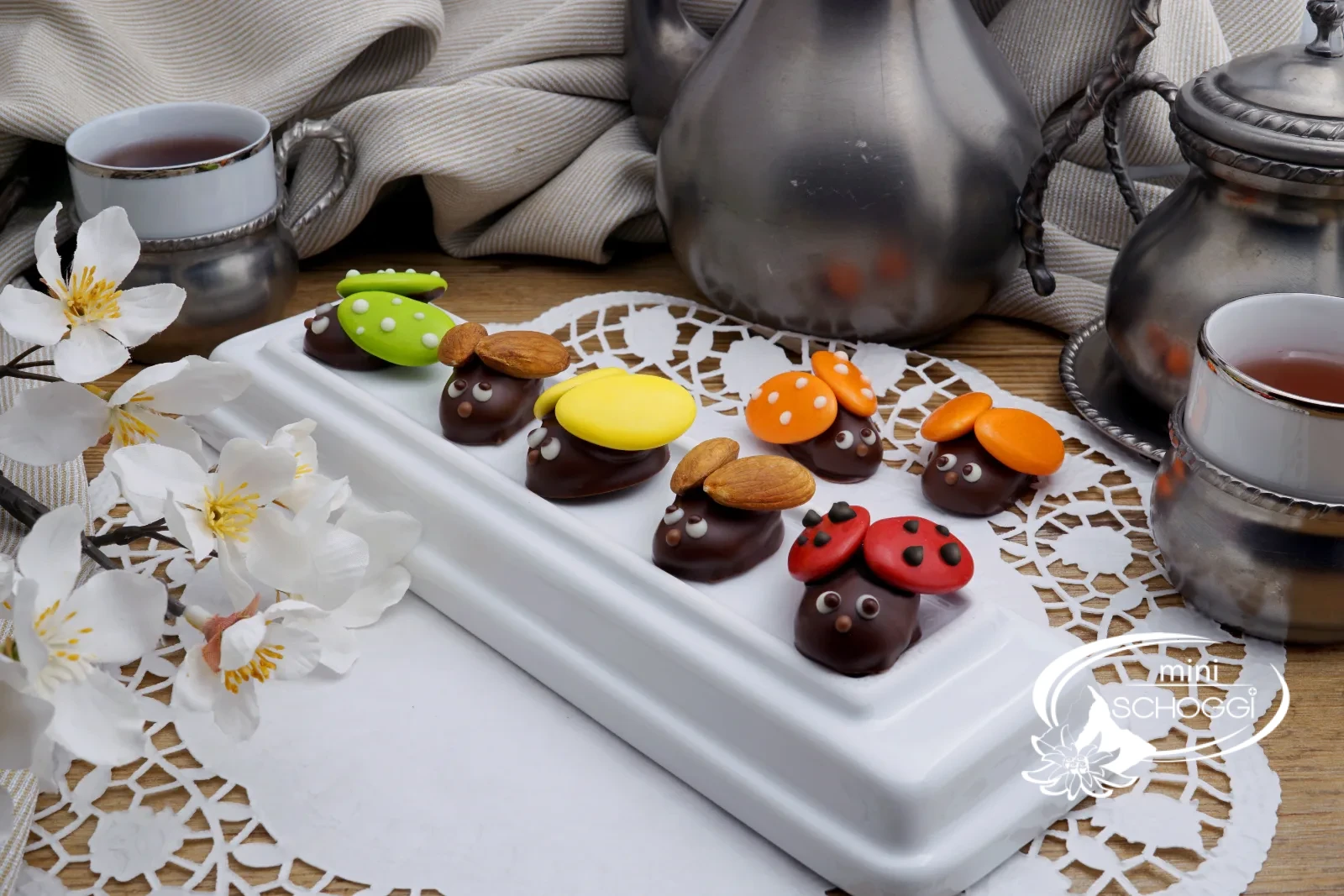 Schoggi-Marienkäfer aus Butterganache auf einer weissen Tortenplatte mit Frühlingsblüten