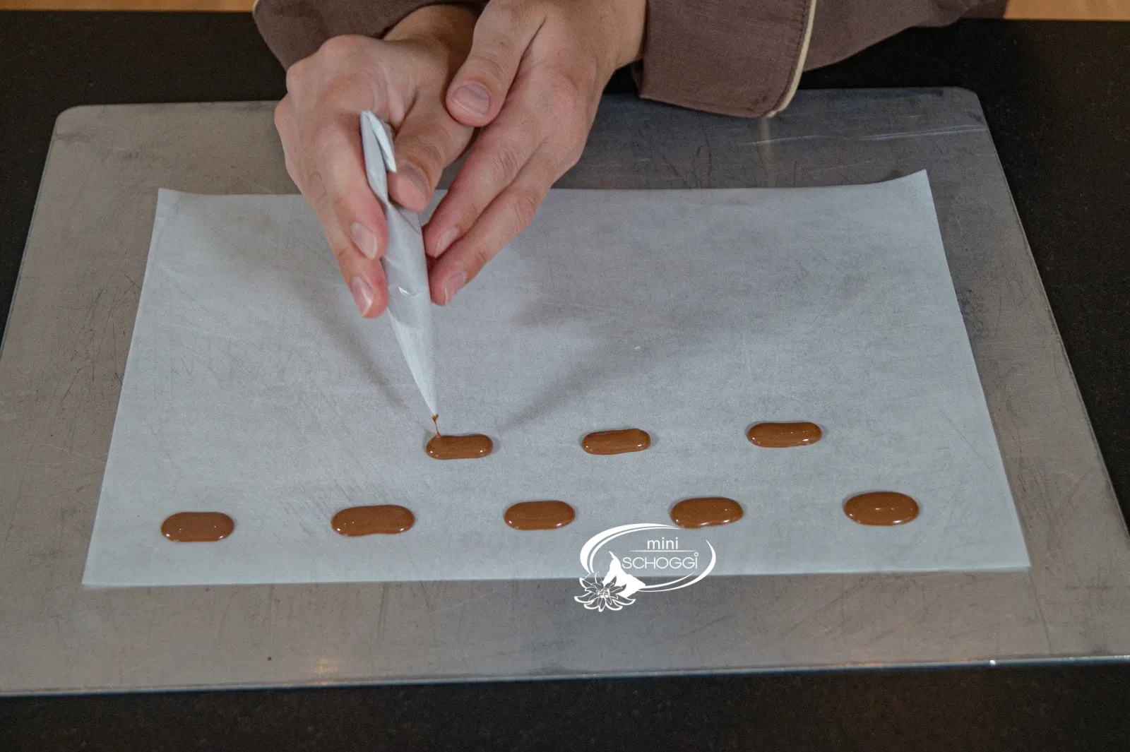 Längliche Couverturedrops werden mit dem Cornet auf Backpapier gespritzt