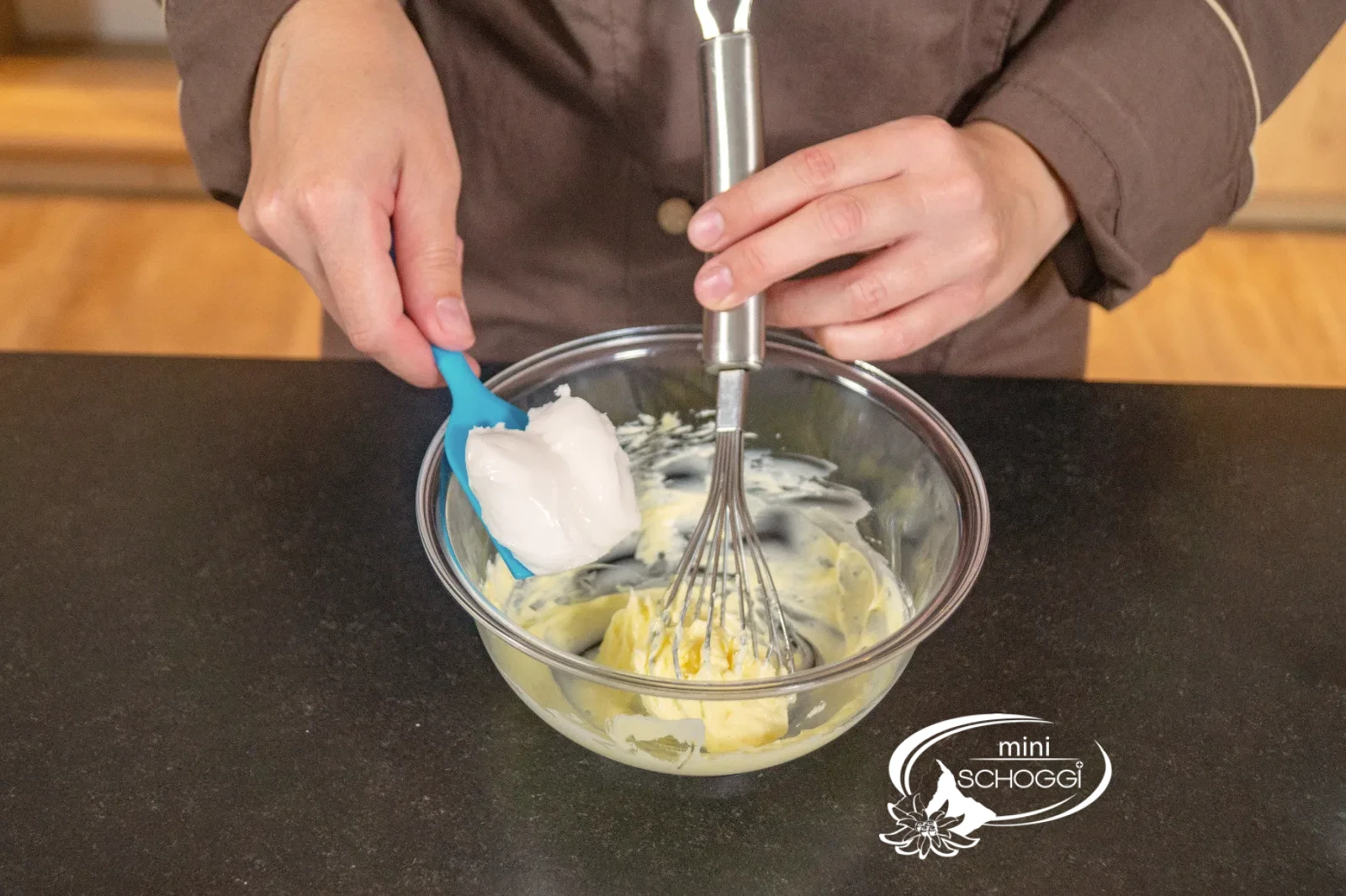 Schmelzfondant wird mit dem Teigschaber zur aufgeschlagenen Butter gegeben