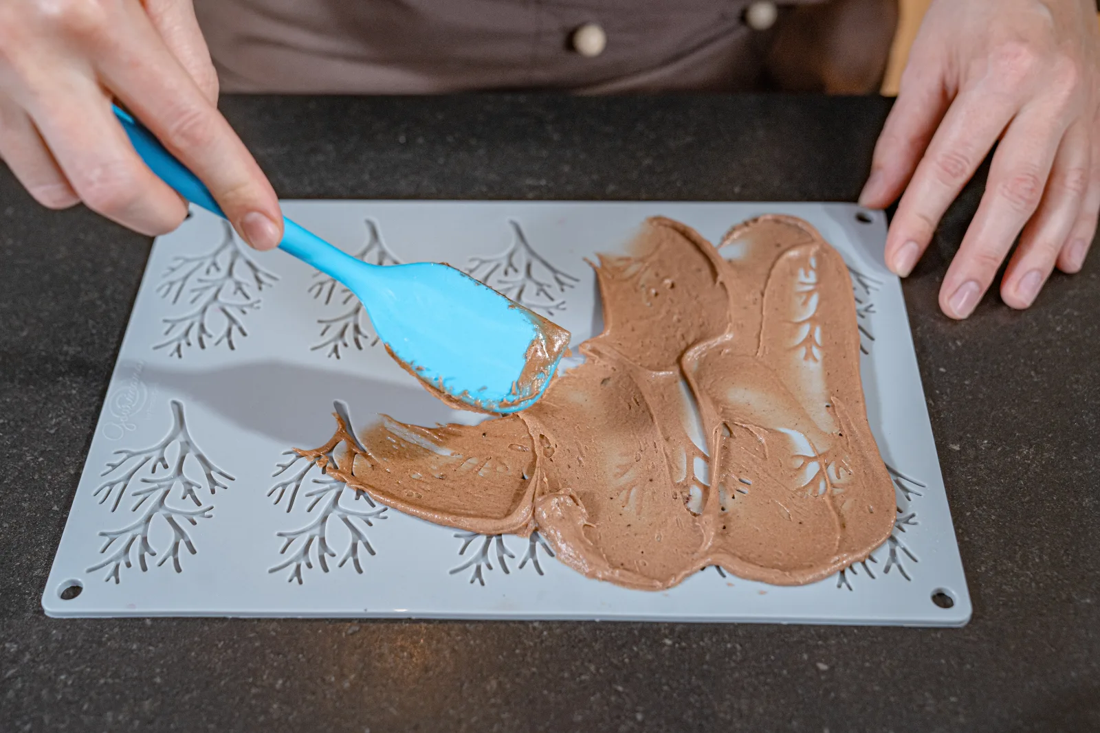 The chocolate mixture is spread into the Hüppen mat with the Rubber scraper