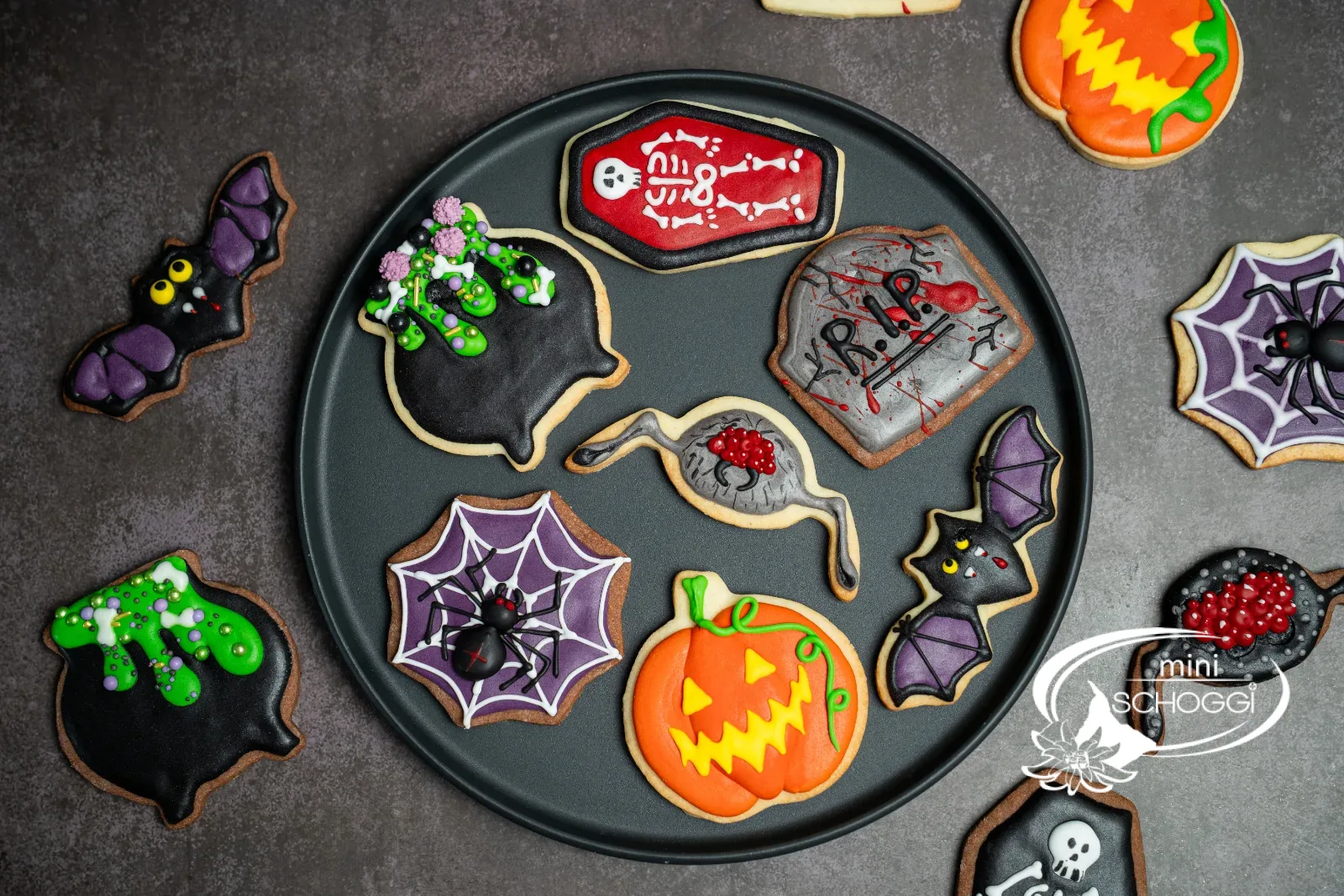 Halloween-Guetzli mit Royal Icing: Kessel, Sarg, Spinnennetz, Kürbis und Grabstein auf einem Teller