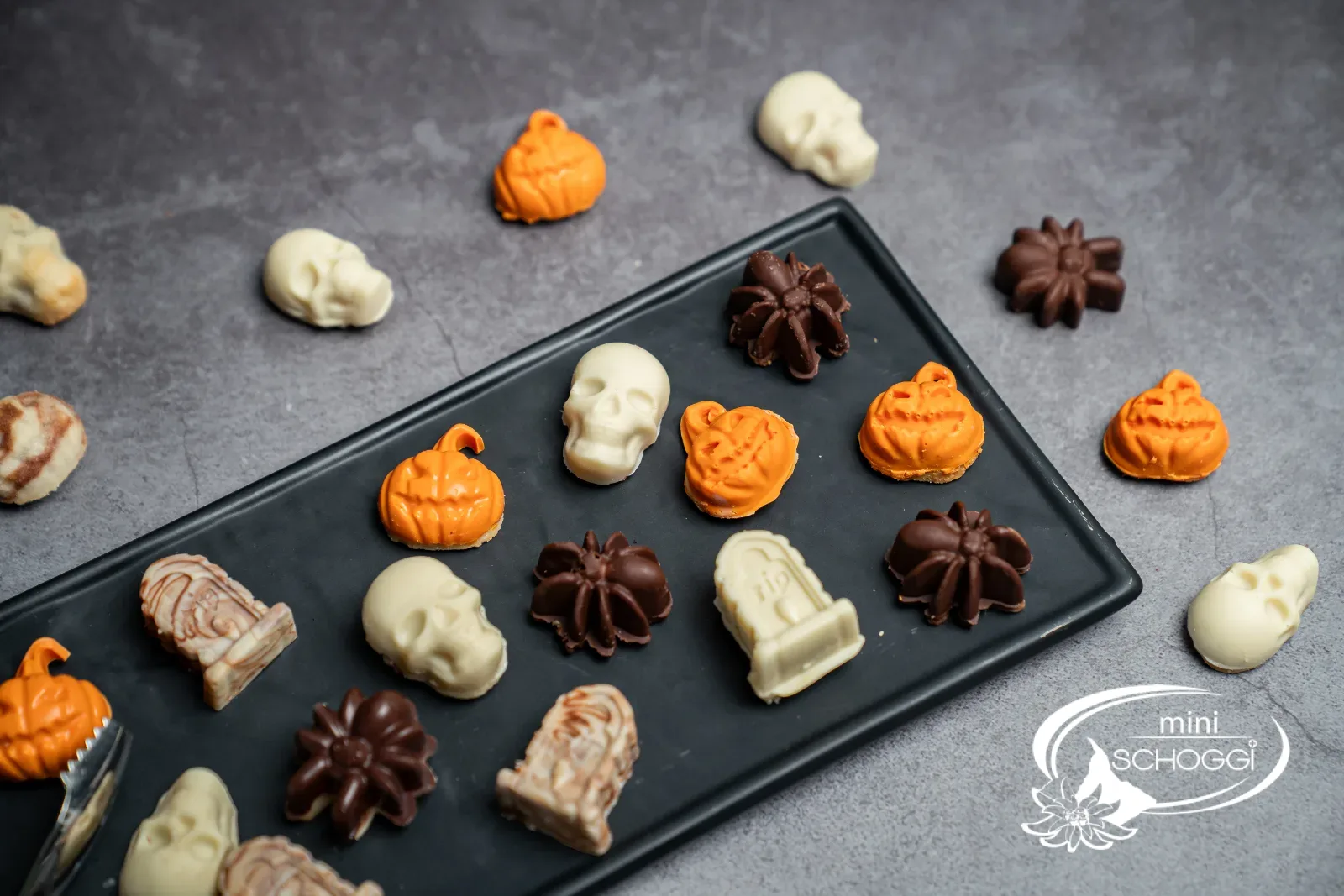 Halloween-Schoggiguetzli als Totenköpfe, Kürbisse, Spinnen und Grabsteine auf einer schwarzen Platte