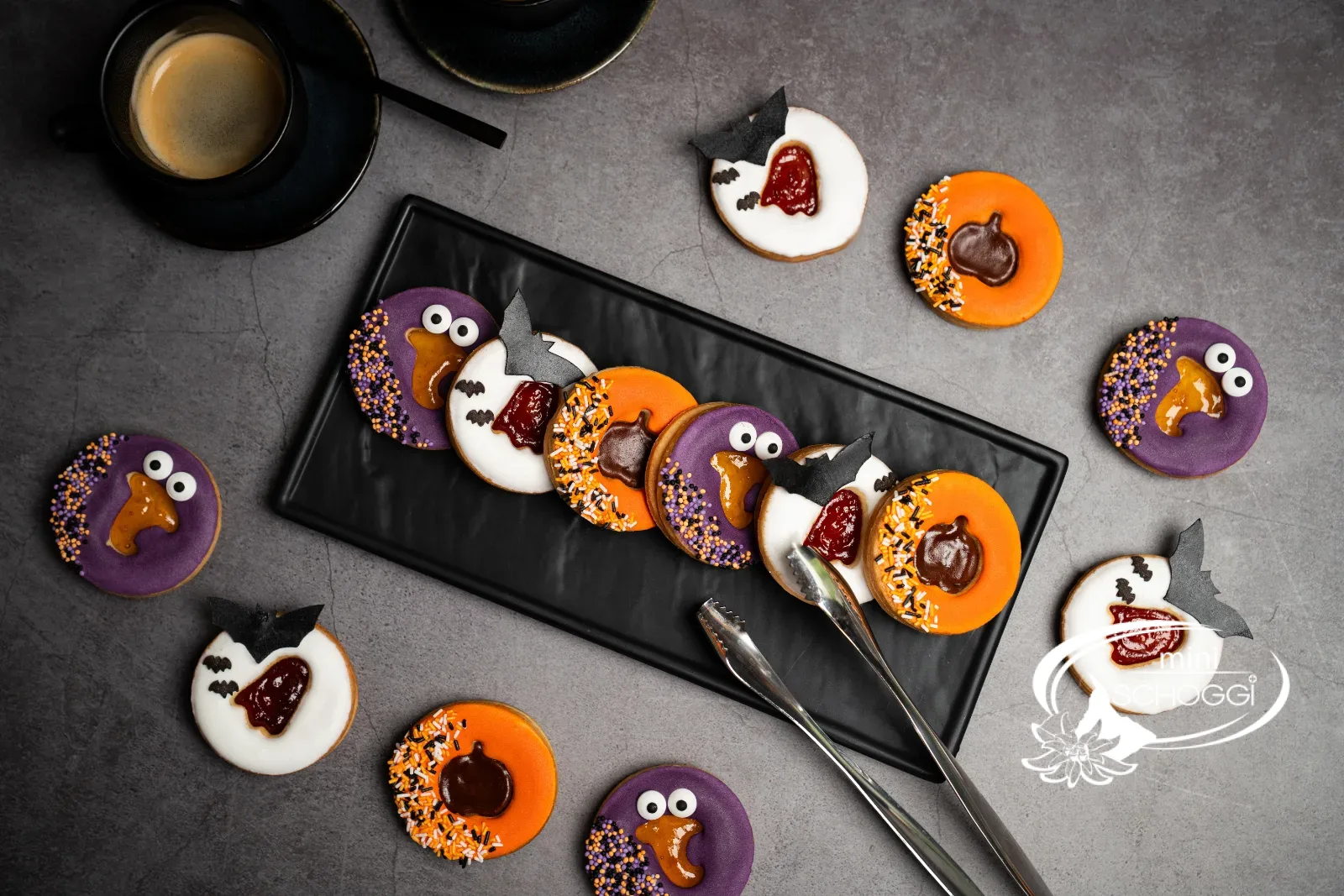 Halloween-Spitzbuben mit oranger, violetter und weisser Glasur auf einem schwarzen Teller