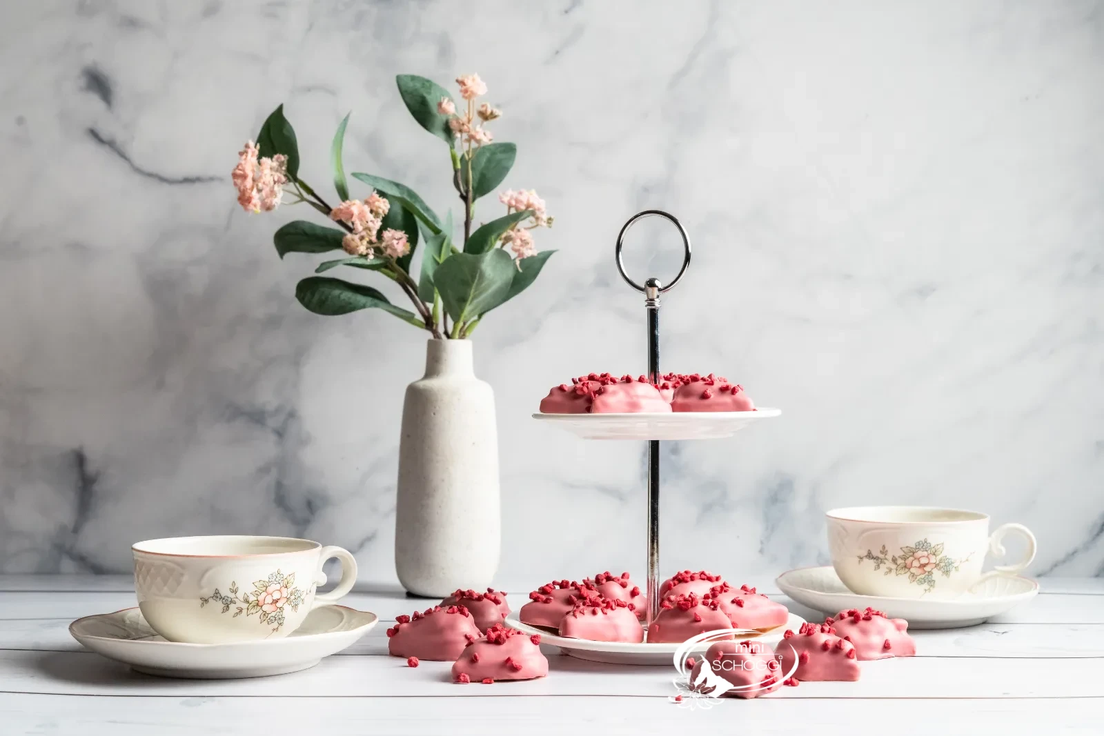 Biscotti a cuore lampone-vaniglia con copertura Ruby su marmo chiaro accanto a una tazza di caffè