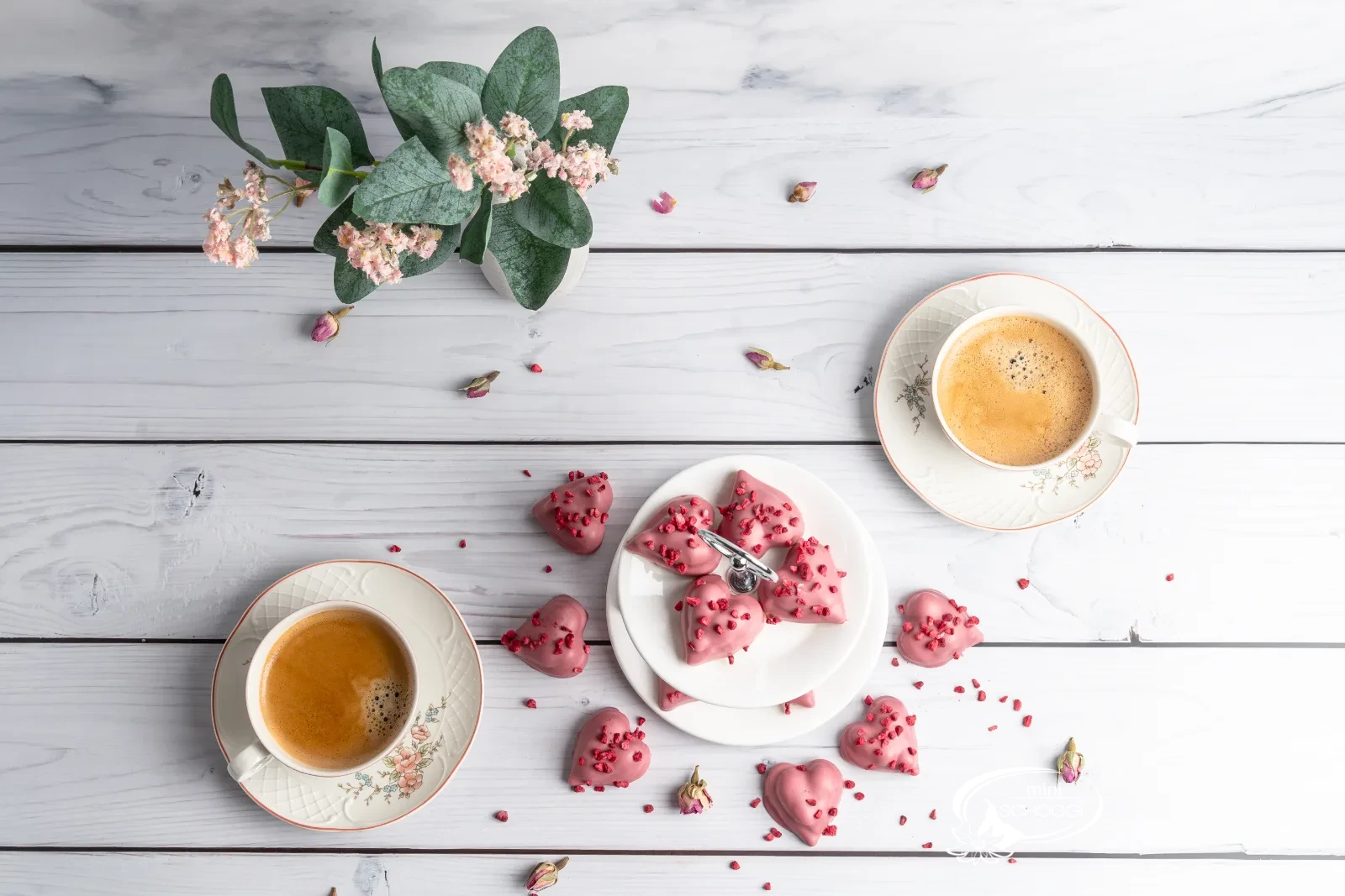 Biscotti a cuore lampone-vaniglia con copertura Ruby su marmo chiaro accanto a una tazza di caffè
