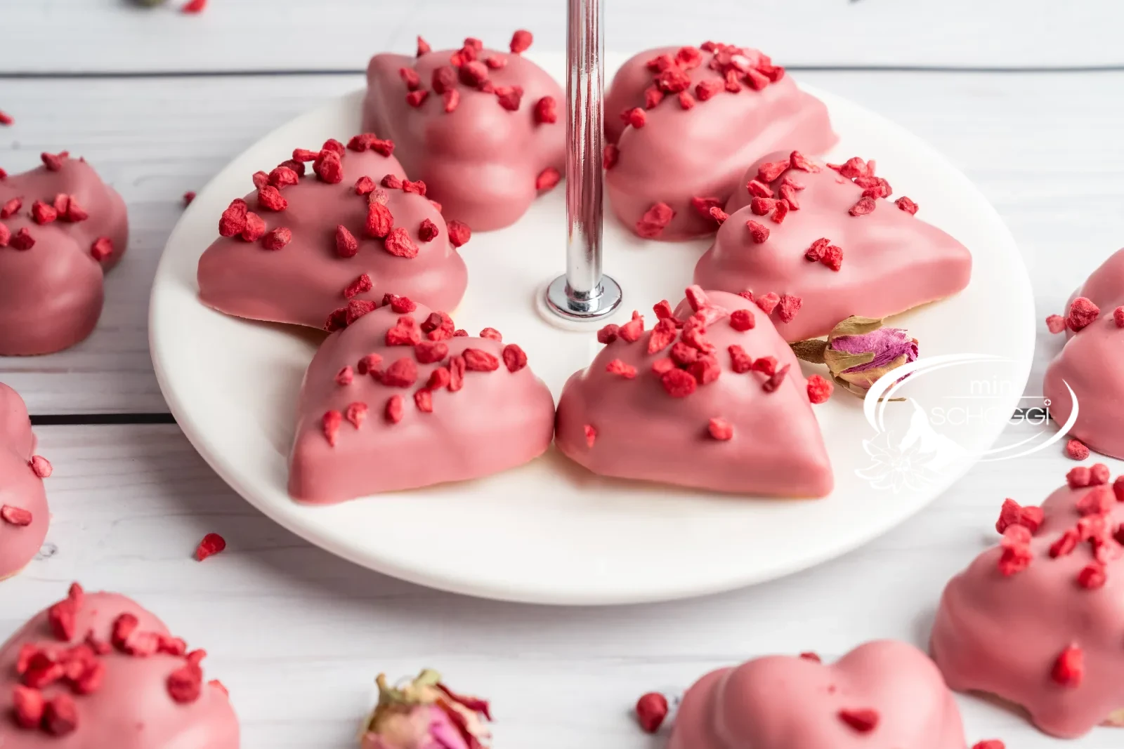 Biscotti a cuore lampone-vaniglia con copertura Ruby su marmo chiaro accanto a una tazza di caffè
