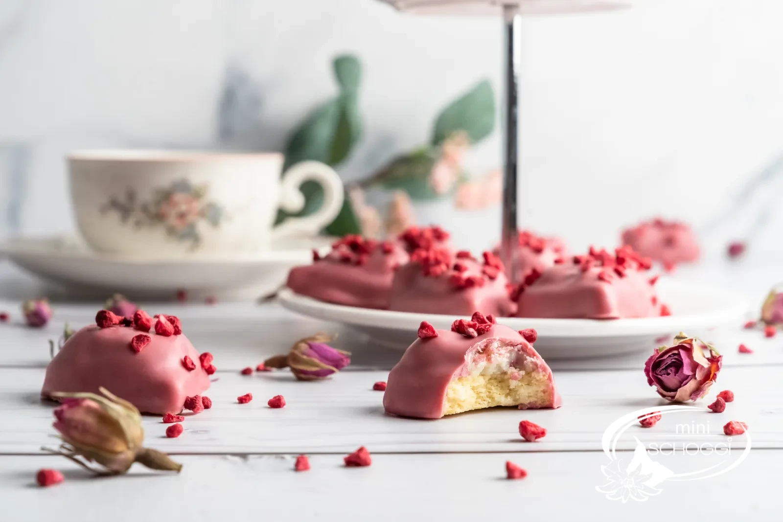 Biscotti a cuore lampone-vaniglia con copertura Ruby su marmo chiaro accanto a una tazza di caffè