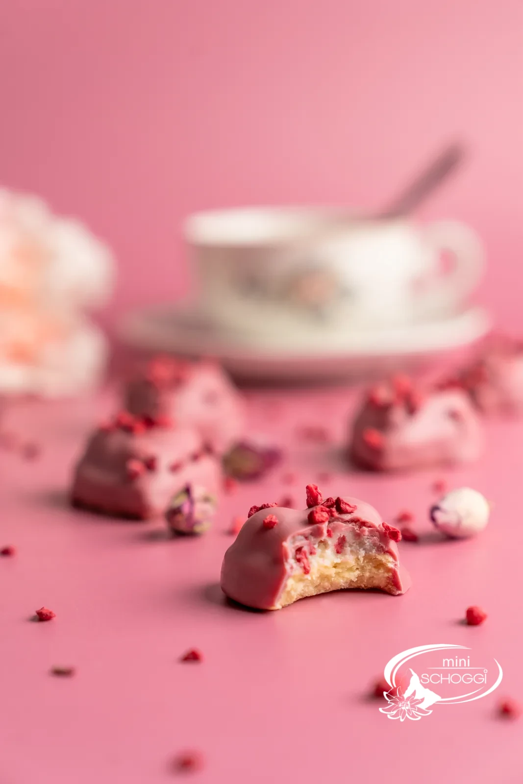 Biscotti a cuore lampone-vaniglia con copertura Ruby su marmo chiaro accanto a una tazza di caffè