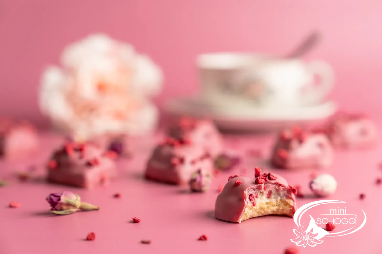 Biscotti a cuore lampone-vaniglia con copertura Ruby su marmo chiaro accanto a una tazza di caffè