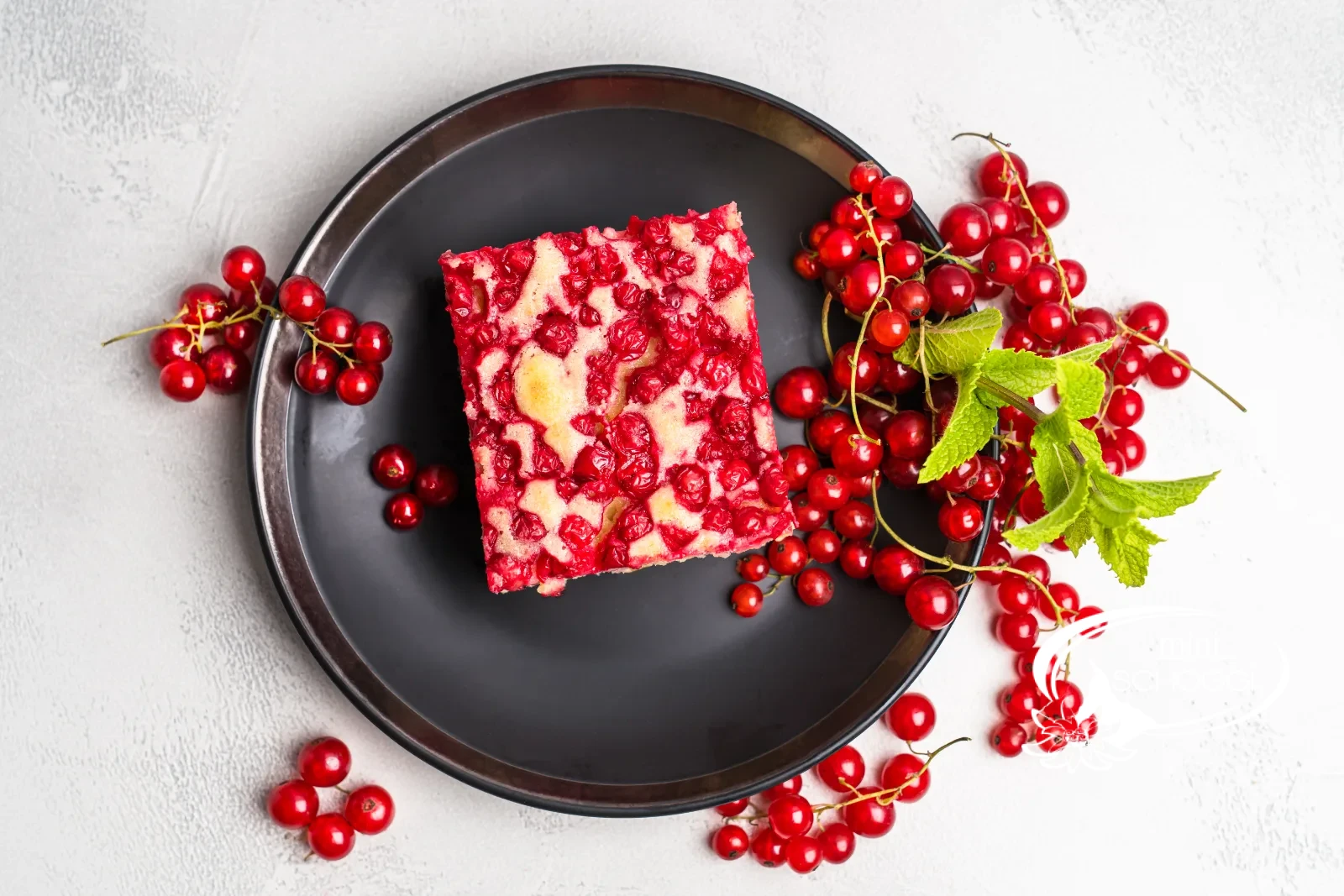 Stück Johannisbeerkuchen von oben auf dunklem Teller, umgeben von frischen Johannisbeeren