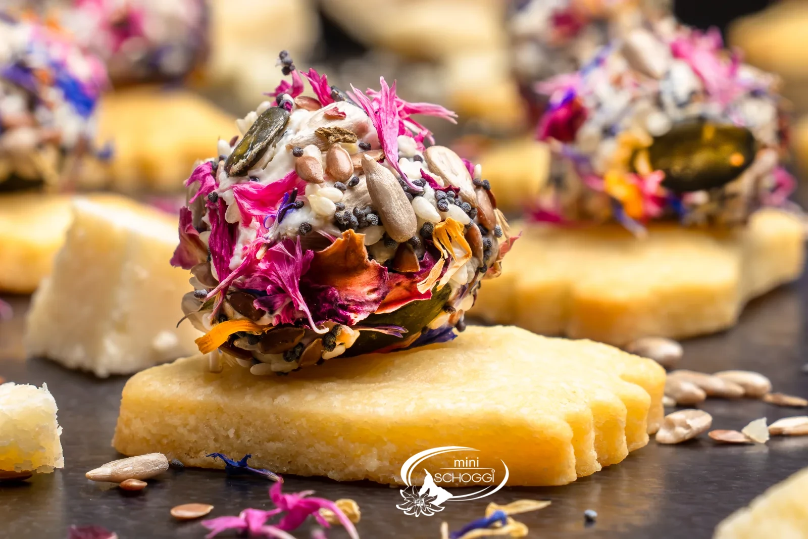 Piedi puzzolenti da aperitivo con palline colorate di formaggio fresco, accanto pezzi di parmigiano e un bicchiere con la miscela di fiori e semi