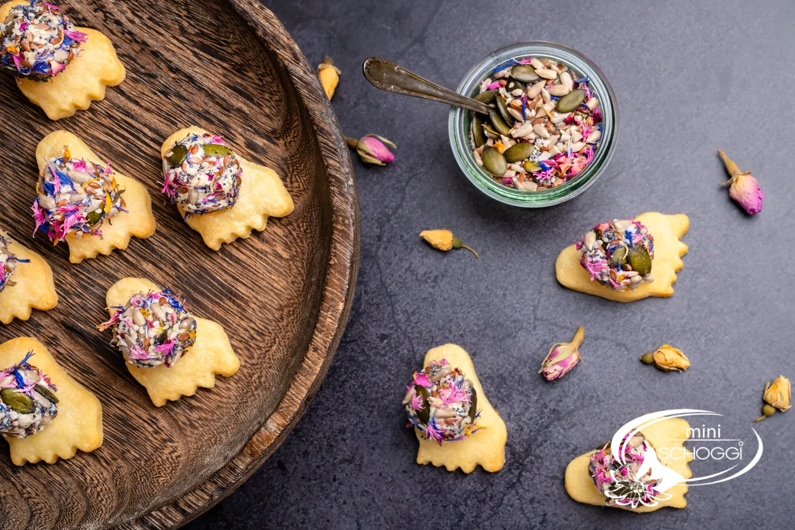 Piedi puzzolenti da aperitivo con palline colorate di formaggio fresco, accanto pezzi di parmigiano e un bicchiere con la miscela di fiori e semi