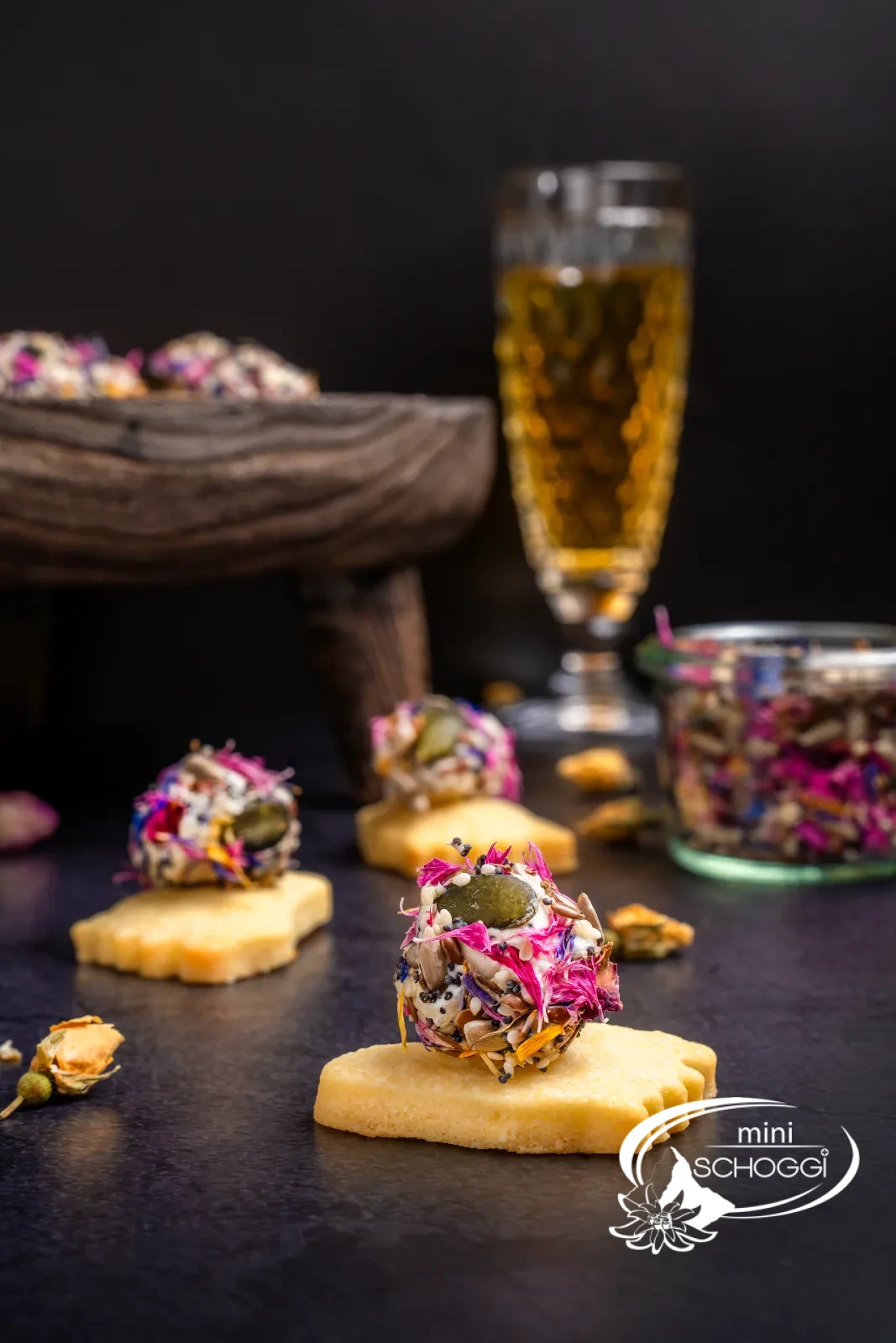 Piedi puzzolenti da aperitivo con palline colorate di formaggio fresco, accanto pezzi di parmigiano e un bicchiere con la miscela di fiori e semi