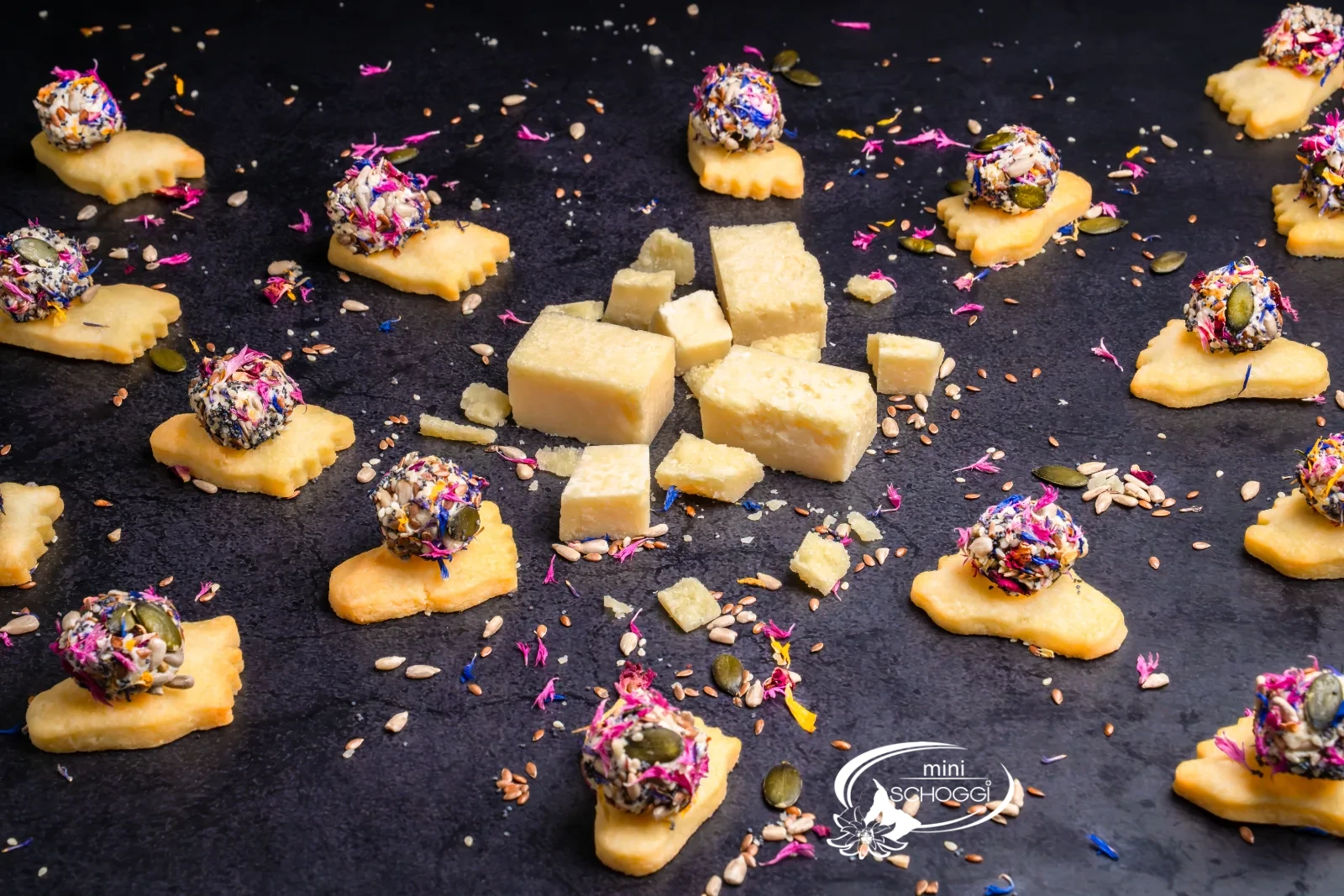 Piedi puzzolenti da aperitivo con palline colorate di formaggio fresco, accanto pezzi di parmigiano e un bicchiere con la miscela di fiori e semi