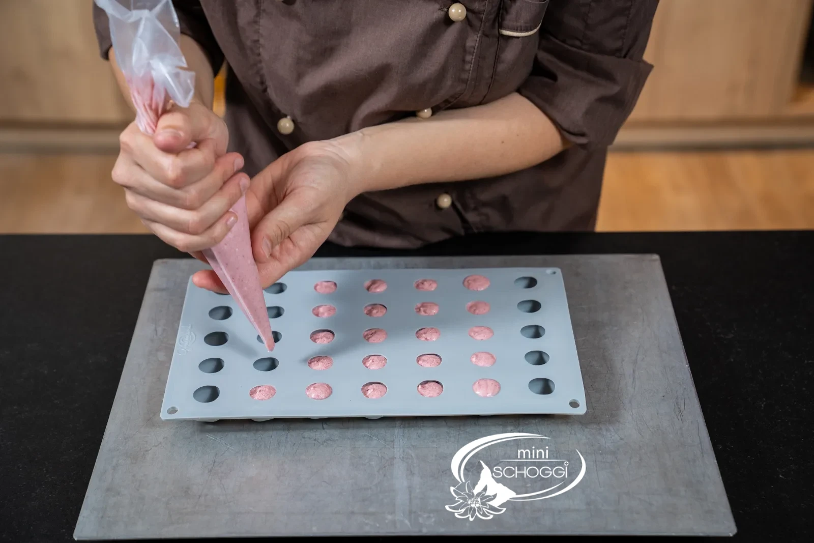 Rosa Mousse wird mit dem Spritzsack in die Mulden einer Silikonform in Kirschenform gefüllt