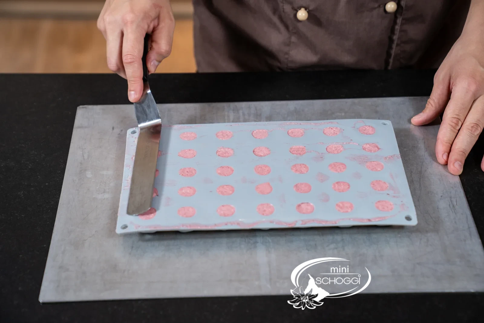 Rosa Mousse wird mit dem Spritzsack in die Mulden einer Silikonform in Kirschenform gefüllt