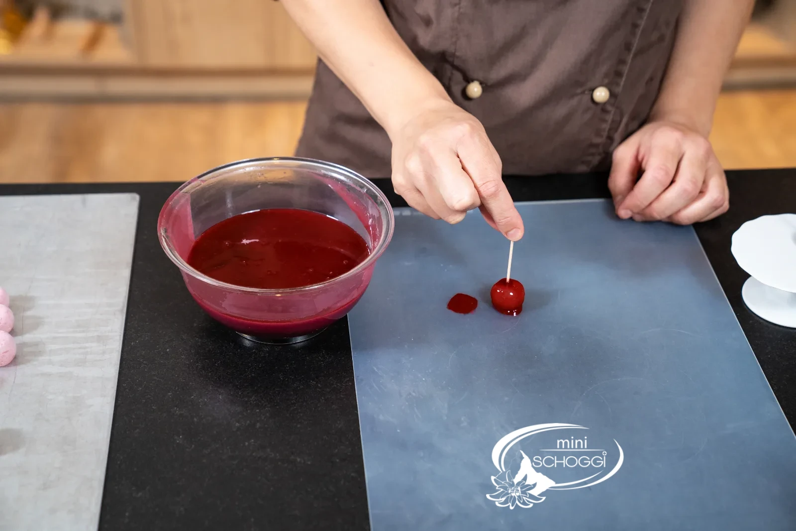 Gefrorene Mousse-Kirsche wird mit einem Spiess in tiefrote Mirror Glaze getaucht, Glasur tropft ab