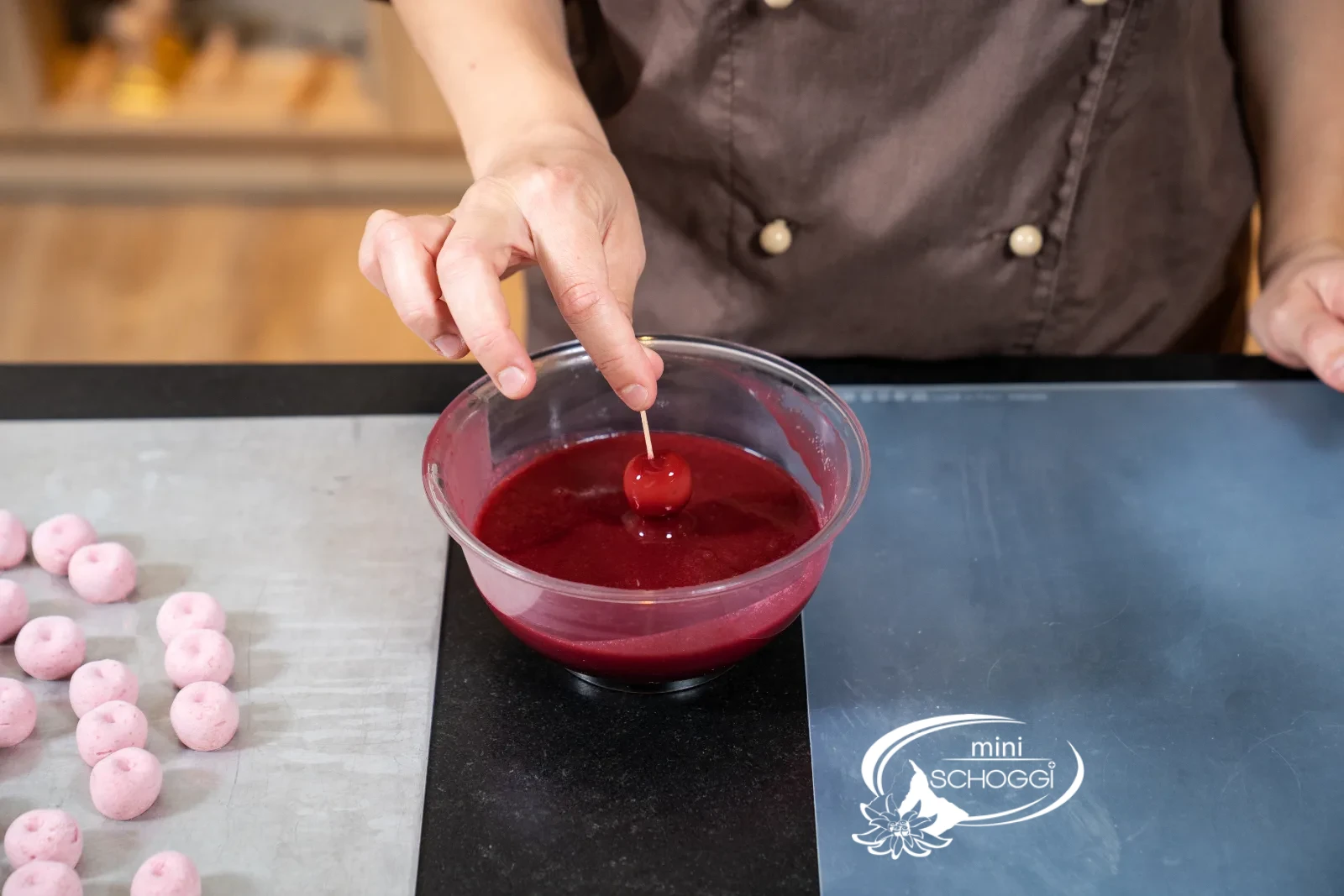 Gefrorene Mousse-Kirsche wird mit einem Spiess in tiefrote Mirror Glaze getaucht, Glasur tropft ab