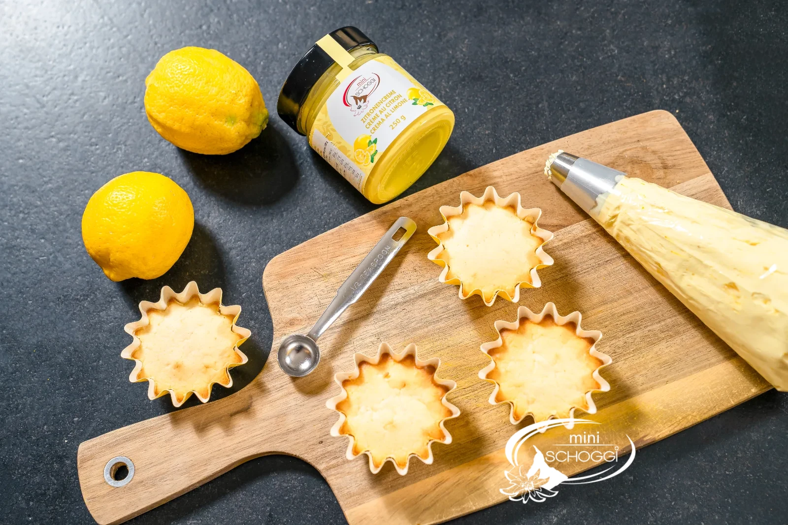 Ausgekühlte Cupcakes neben dem Glas miniSchoggi Zitronencreme und dem Ausstecher