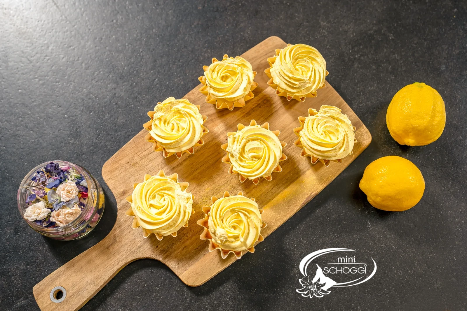 Fertige Lemon Cupcakes mit Frosting und essbaren Blüten auf der Servierplatte