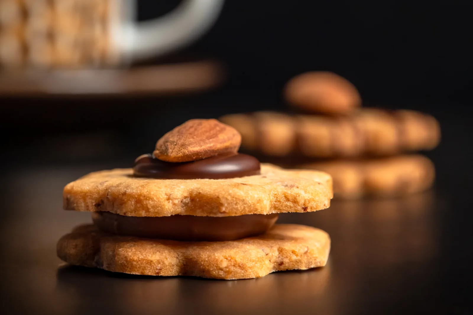 Biscotti con le mandorle impilati con ripieno di Gianduja davanti a una tazza di caffè