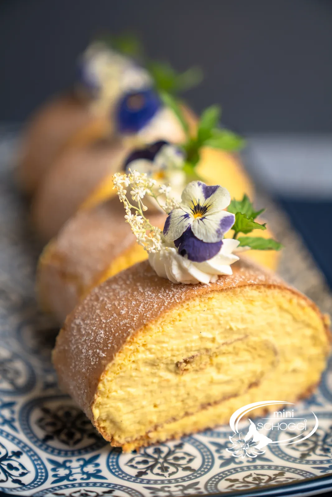 Rotolo al mango e cocco decorato con rosetta di panna, fiori e menta