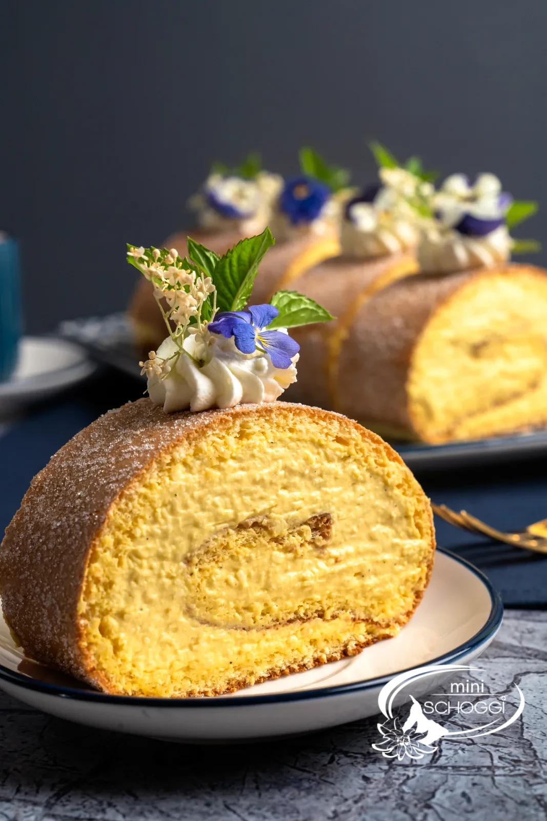 Rotolo al mango e cocco decorato con rosetta di panna, fiori e menta