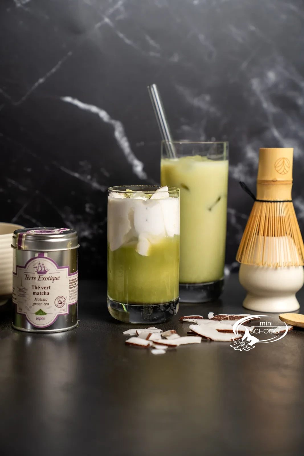 Matcha iced latte in a tall glass with a straw, next to the bamboo whisk
